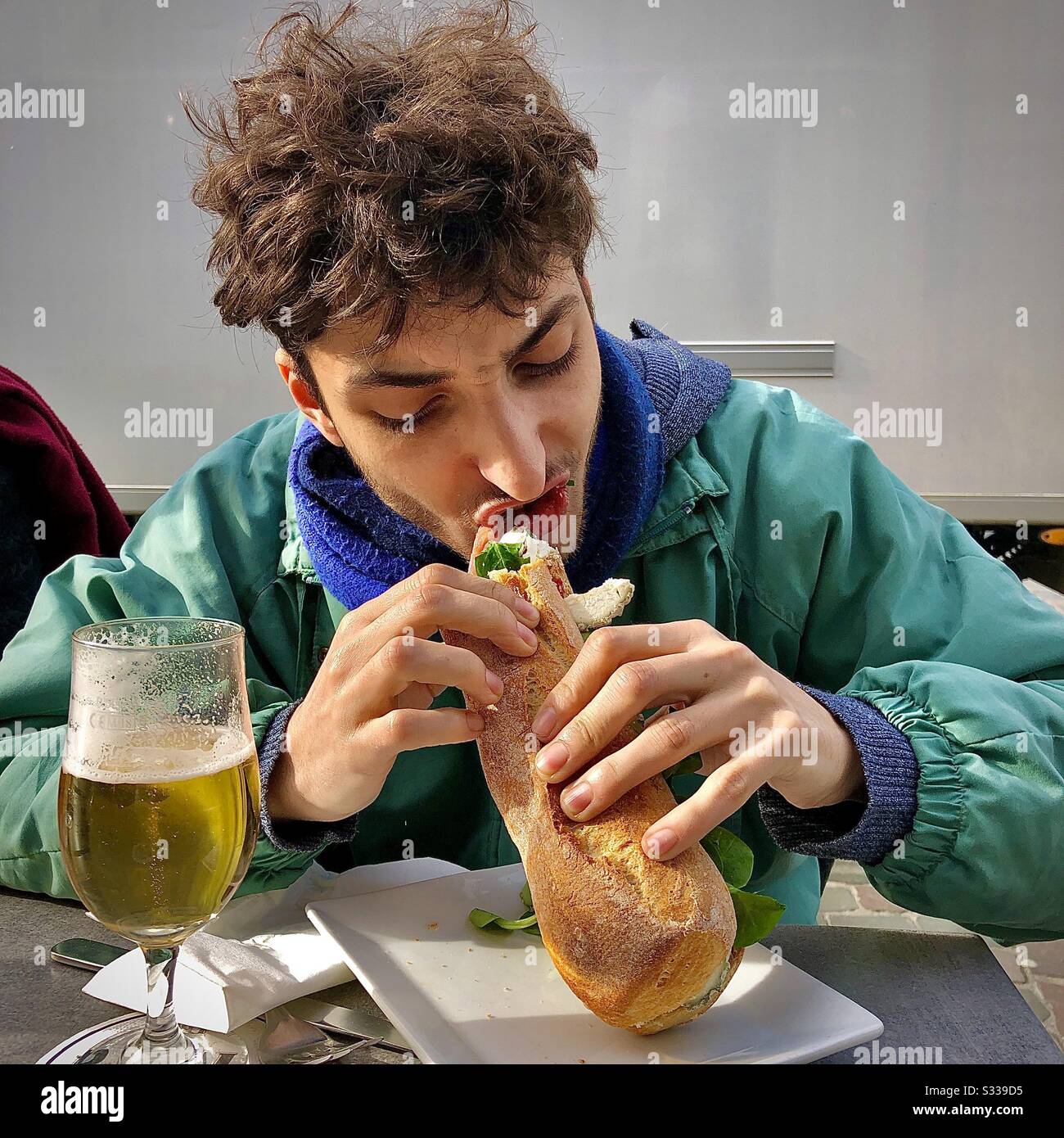 Junger Mann, der ein Baguette-Sandwich isst. Stockfoto