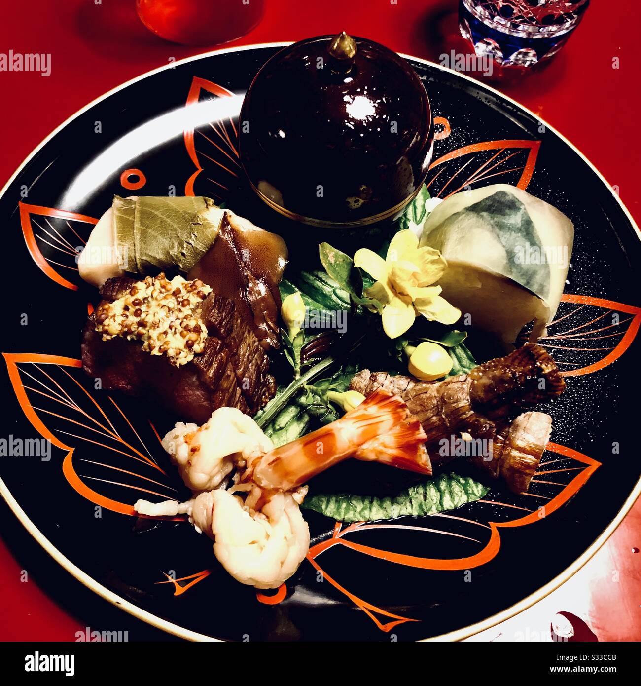 Ein traditionelles japanisches Gänseki-Menü: Gegrillte Garnelen, Baf, Sushi und Gemüse auf einem lackierten Gericht - Smartphone-aufgenommenes Stockfoto
