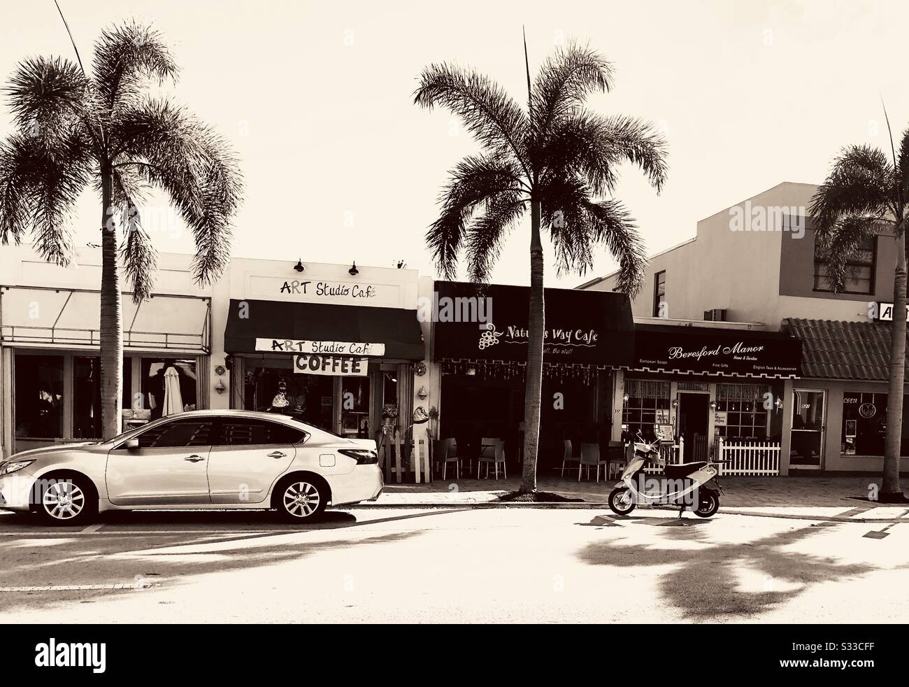 Straßenszene im Stadtzentrum von Lake Worth Beach, Florida mit Palmen, Geschäften, einem Auto und einem Motorrad. - Smartphone-aufgenommenes Stockfoto