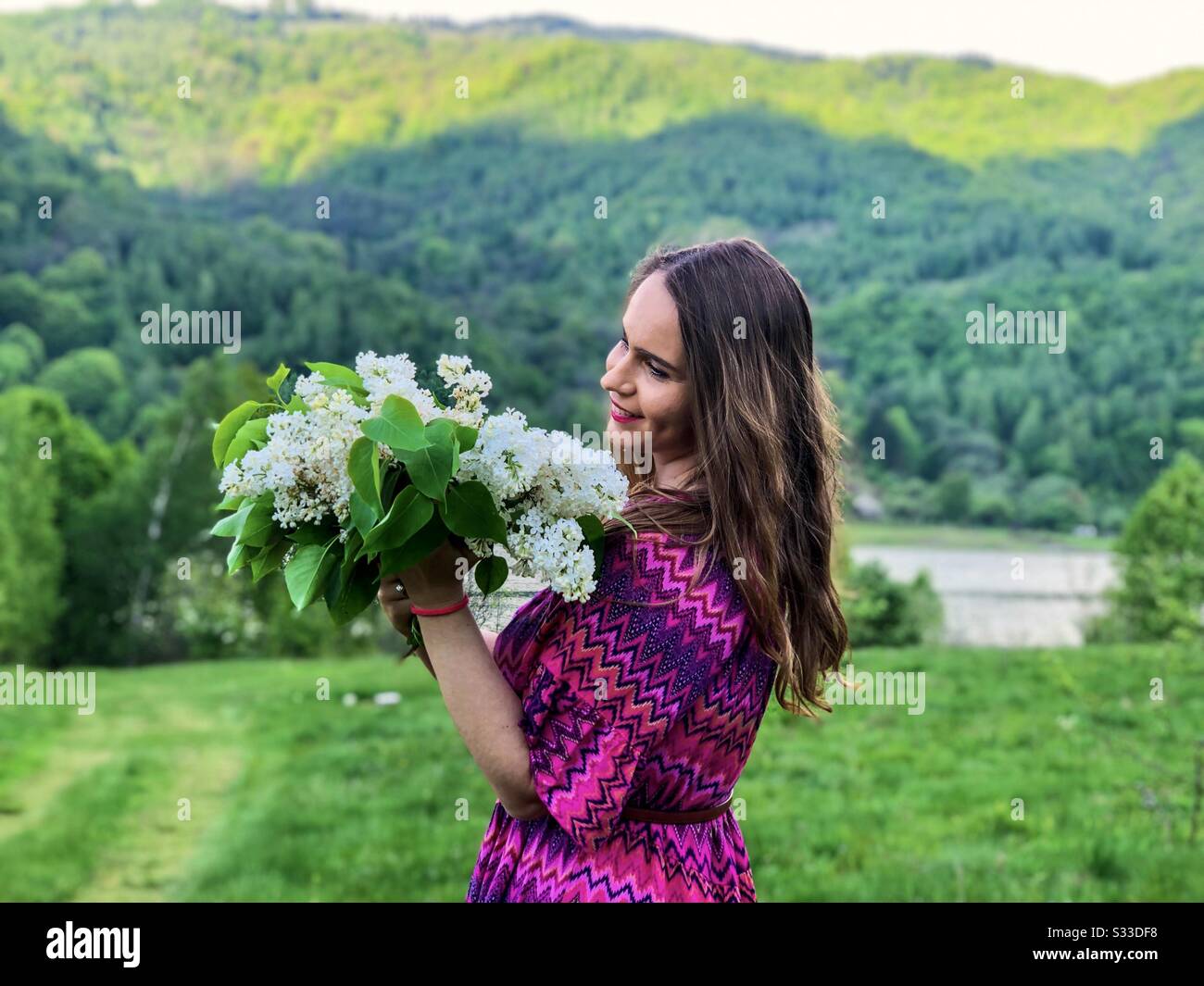 Frau in rosafarbenem Kleid mit einem Blumenstrauß weißer Flieder Stockfoto