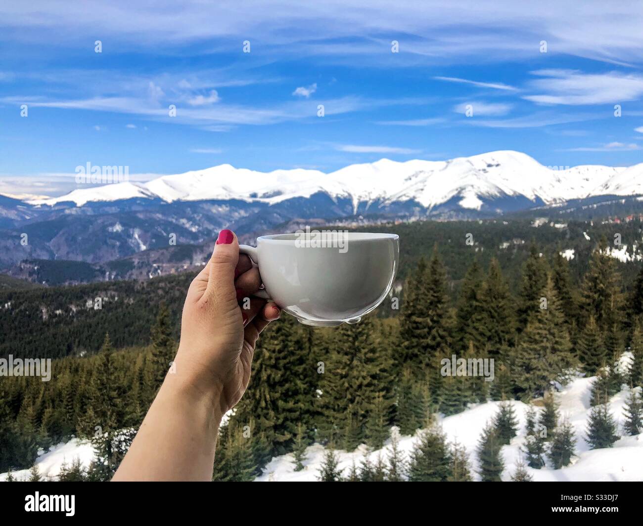 Hand halten Tasse Kaffee mit schneebedeckten Bergen im Hintergrund - Smartphone-aufgenommenes Stockfoto