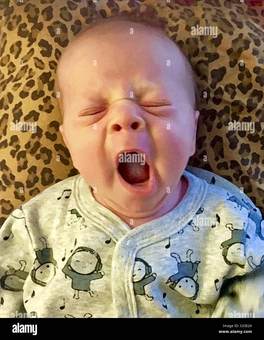 Babyjungen, die gegen eine mit Leoparden gemusterte Decke gähnen. - Smartphone-aufgenommenes Stockfoto