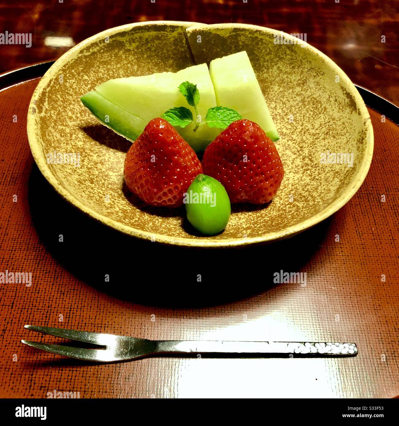 Zwei Erdbeeren, ein Stück Melone, Yamamomo-Früchte (japanische Bajbeere) und Minzblätter auf einer Keramikplatte, Dessert serviert in einem japanischen traditionellen Ryokan in Kyoto - Smartphone-aufgenommenes Stockfoto