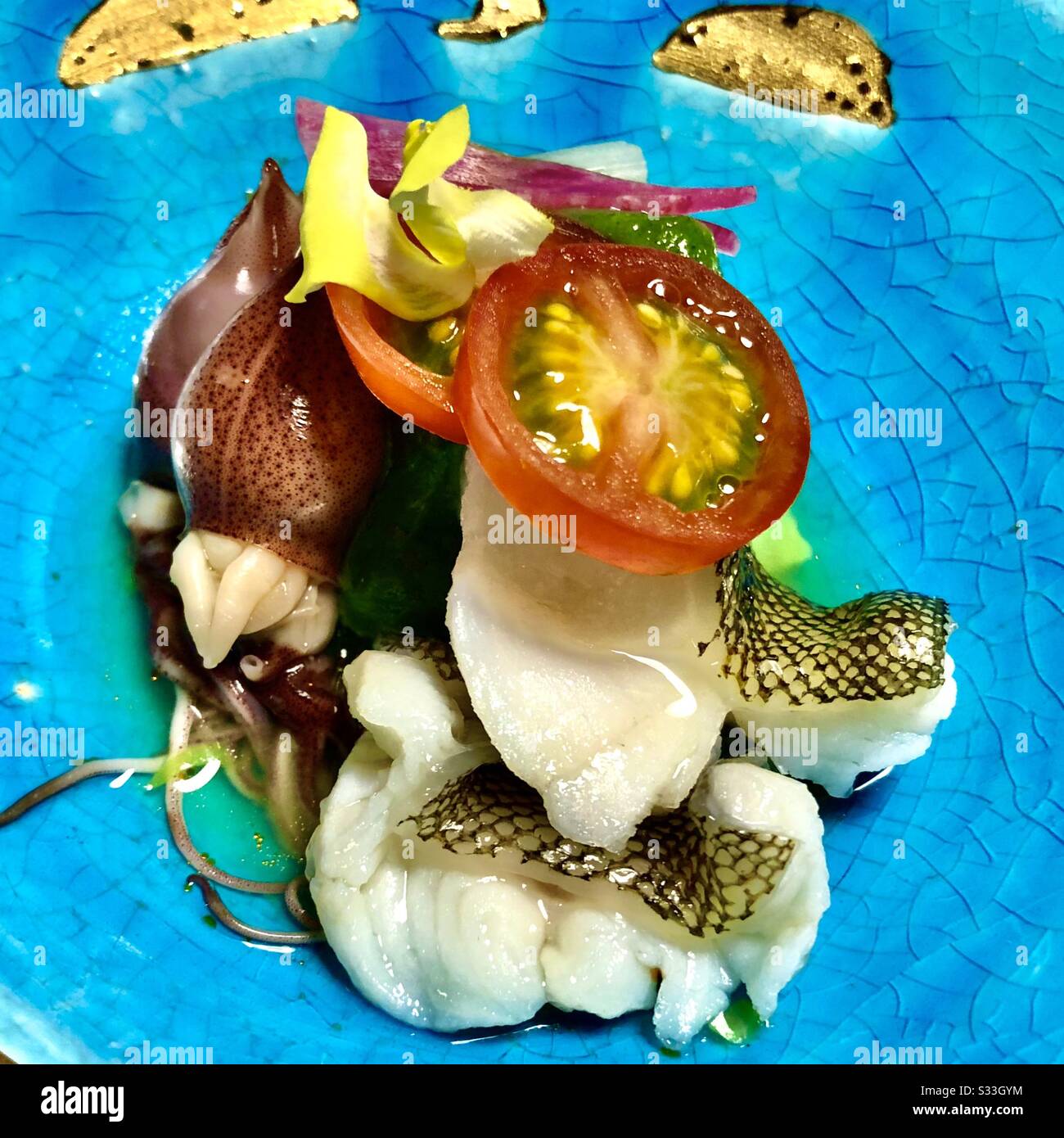 Hotaru ika (Feuergefecht) und hamo Fish (Daggertooth Hike Conger) mit einer Scheibe Kirschtomate. Kaiseki-Gericht serviert auf einer blauen, mit Zölissin gerissenen Porzellanplatte mit Kintsugi. Kyoto, Japan - Smartphone-aufgenommenes Stockfoto