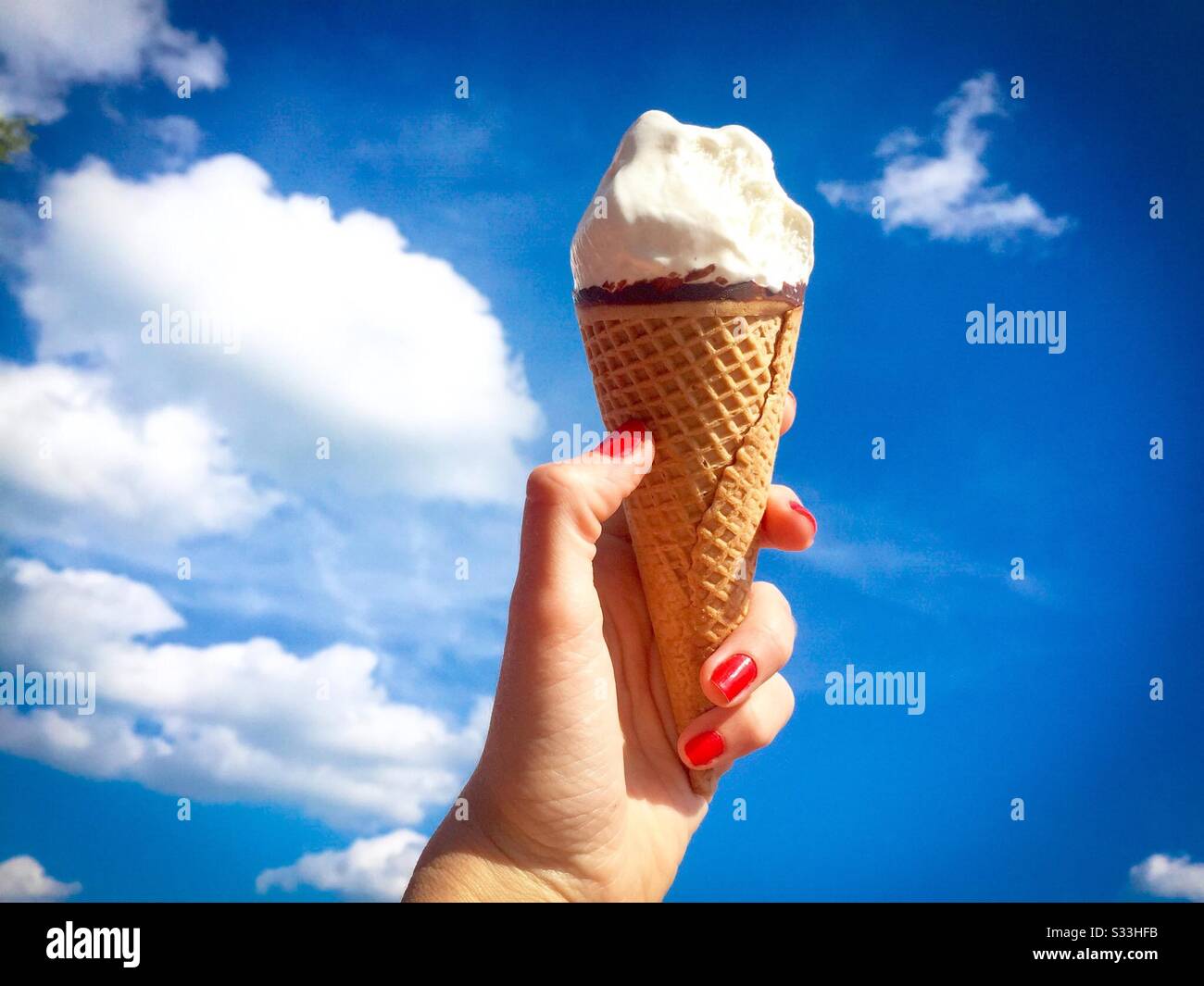 Hand, die den Vanilleeiskegel am Himmel hält Stockfoto