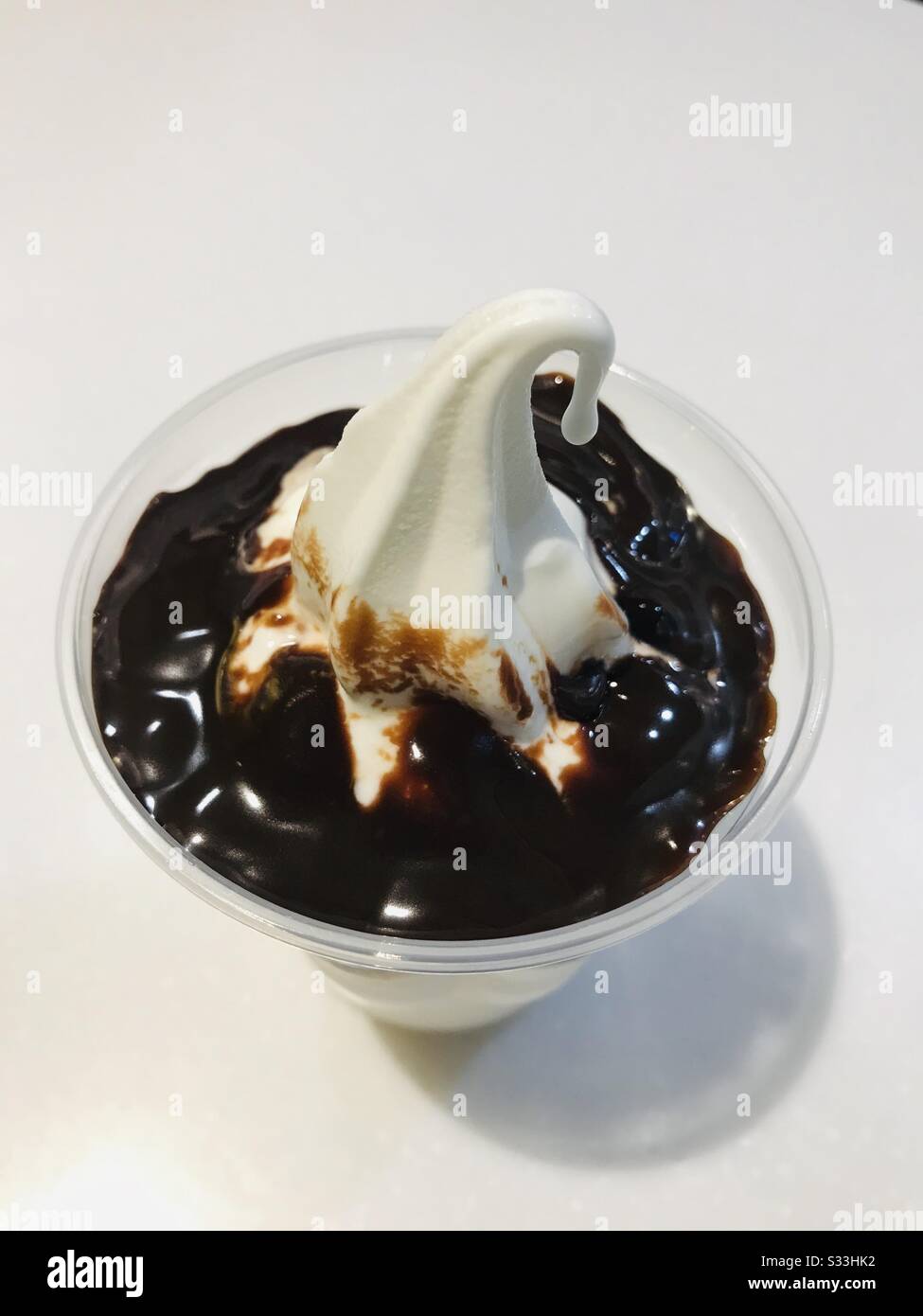 Schokoladen-Fudge-Eis, das vor dem Verkosten auf dem Tisch aufbewahrt wurde, nahm eine Schnapp-Vanille-Eiscreme, Kegeleis in einer transparenten Tasse auf weißem Tisch - Nahaufnahme eines Desserts Stockfoto