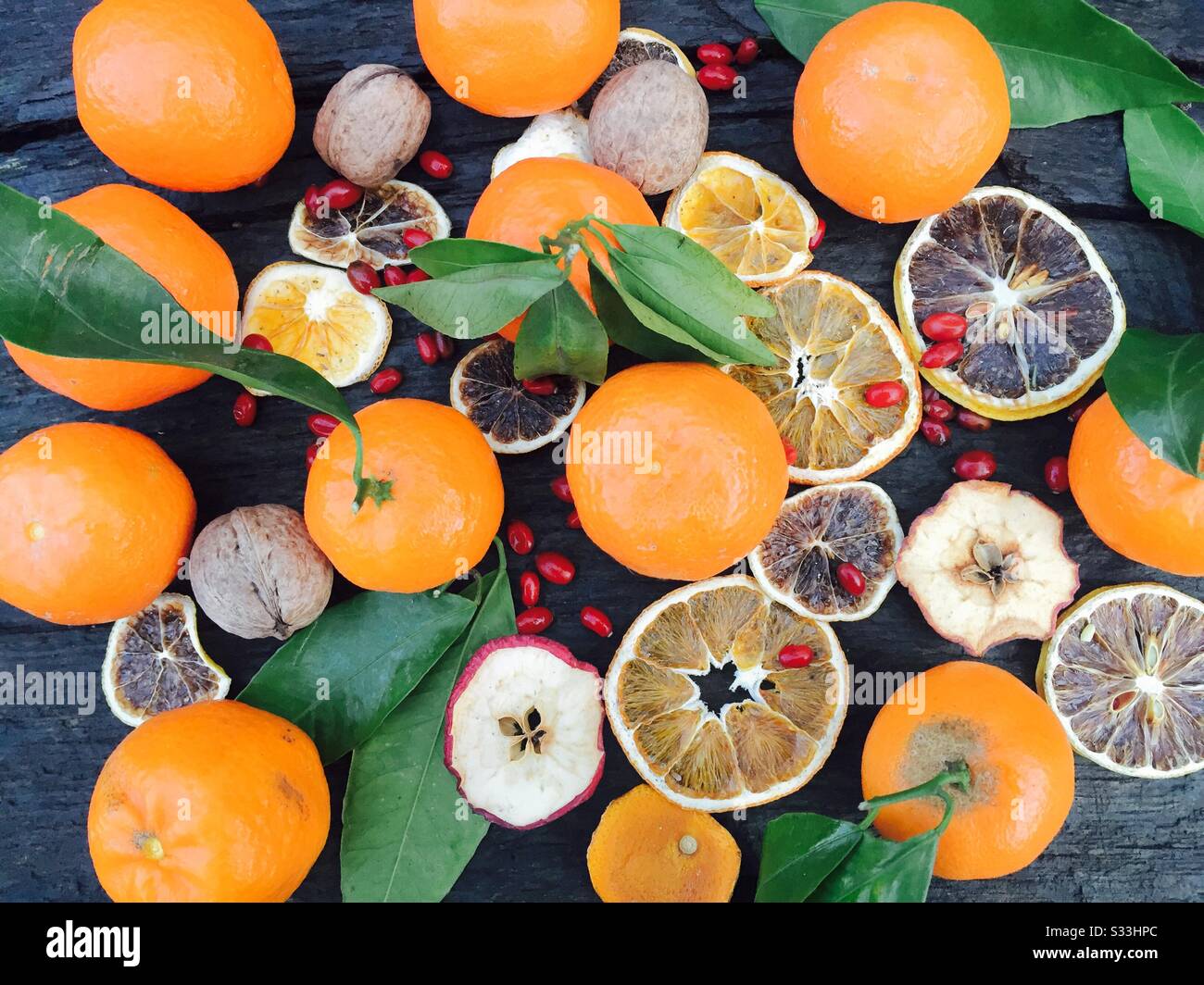 Flache Mandarinen mit roten Beeren und trockenen Früchten wie apfelscheiben, orangefarbene Scheiben auf rustikalem Holztisch Stockfoto