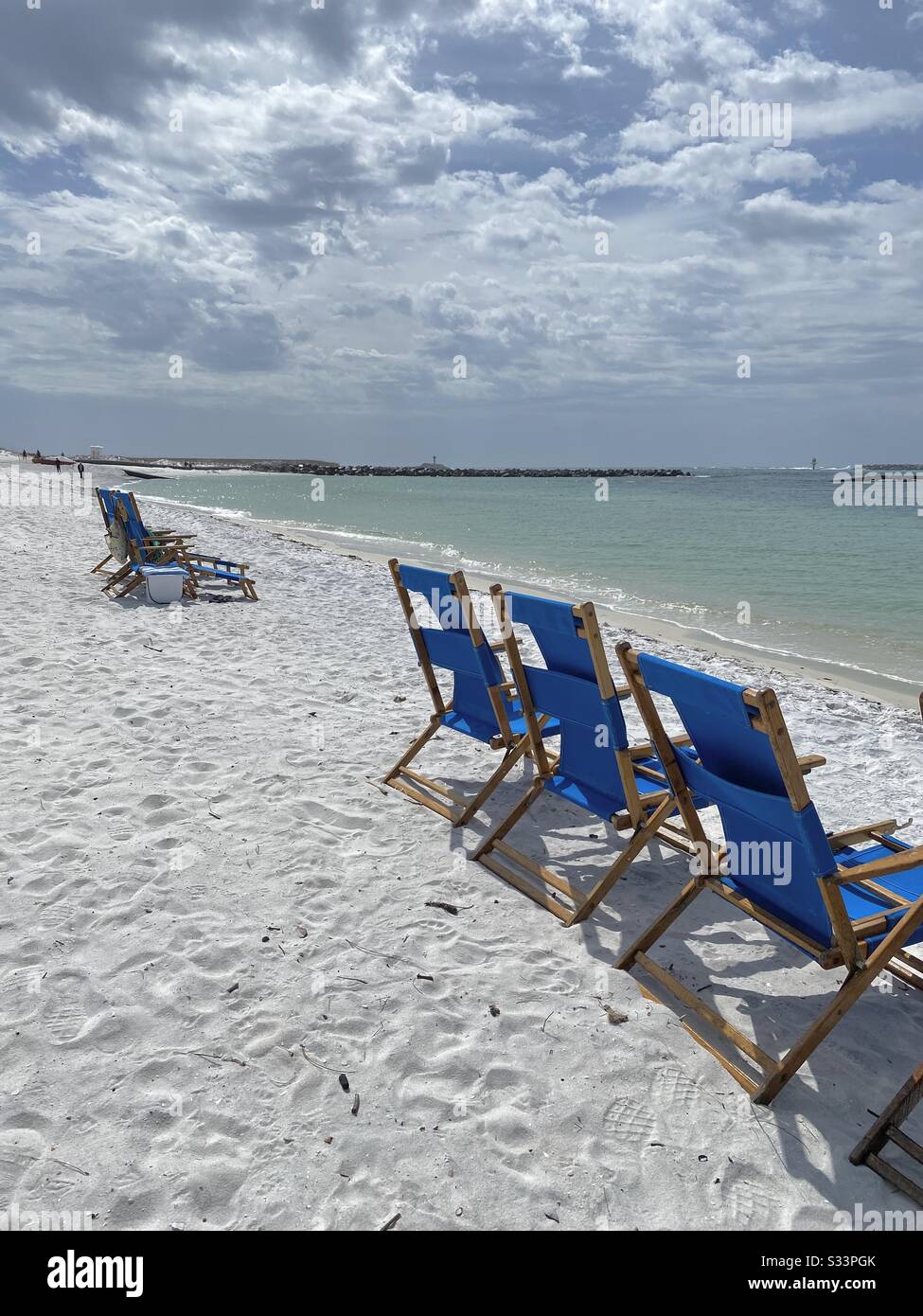 Reihe von leuchtend blauen Stühlen am weißen Strand mit Blick auf das smaragdgrüne Wasser des Golfs von Mexiko - Smartphone-aufgenommenes Stockfoto