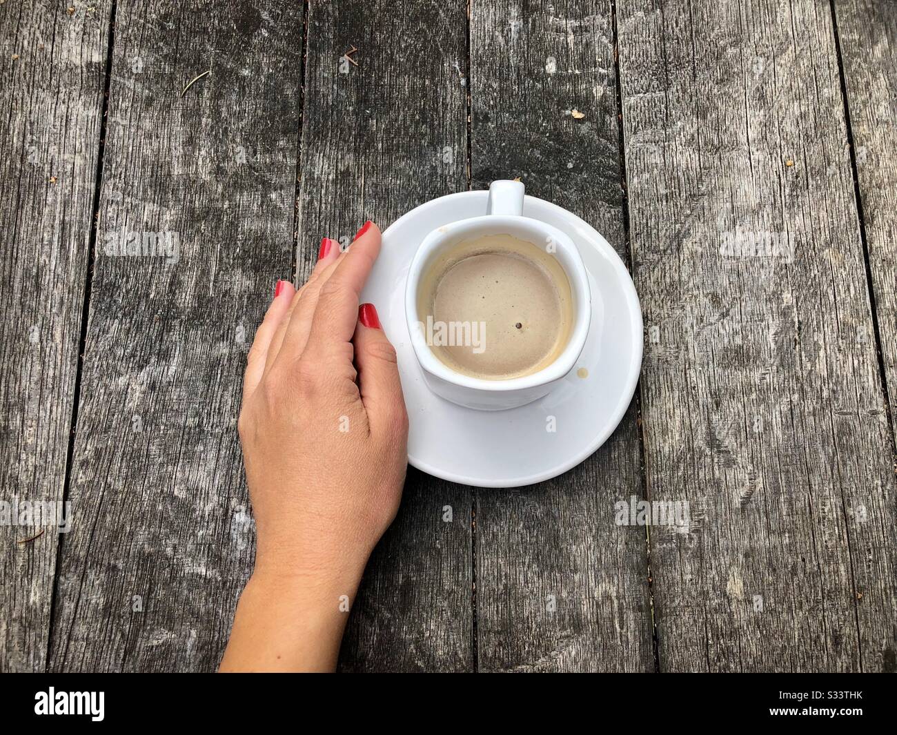Hand der Frau neben der Tasse Kaffee auf rustikalem Holztisch Stockfoto
