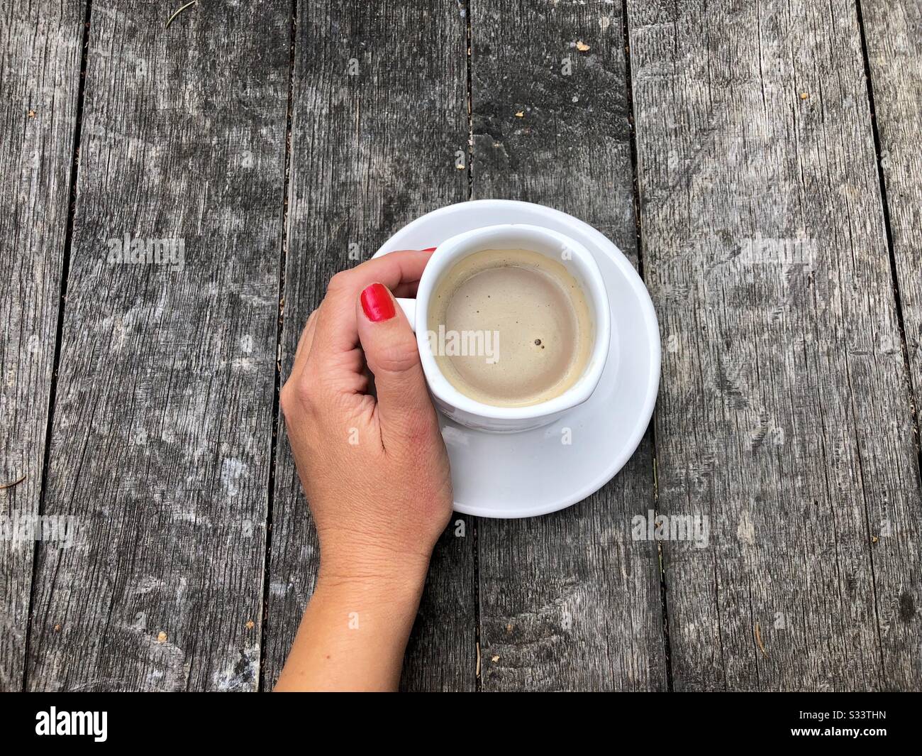 Hand der Frau neben der Tasse Kaffee auf rustikalem Holztisch Stockfoto
