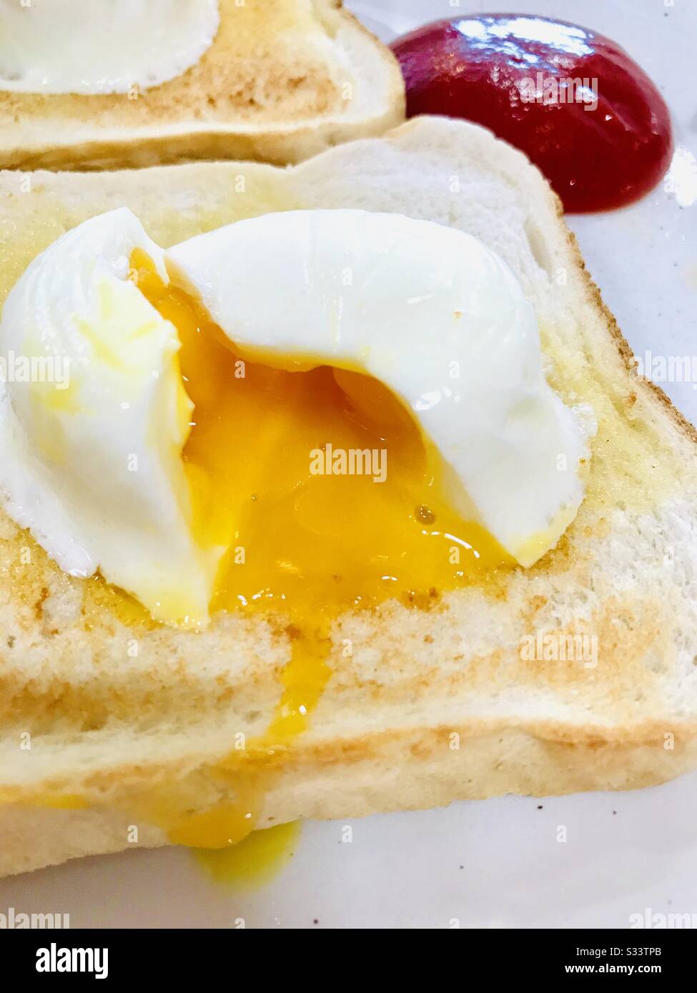 Perfektes runny pochiertes Ei auf Toast mit Tomatensauce im Hintergrund Stockfoto