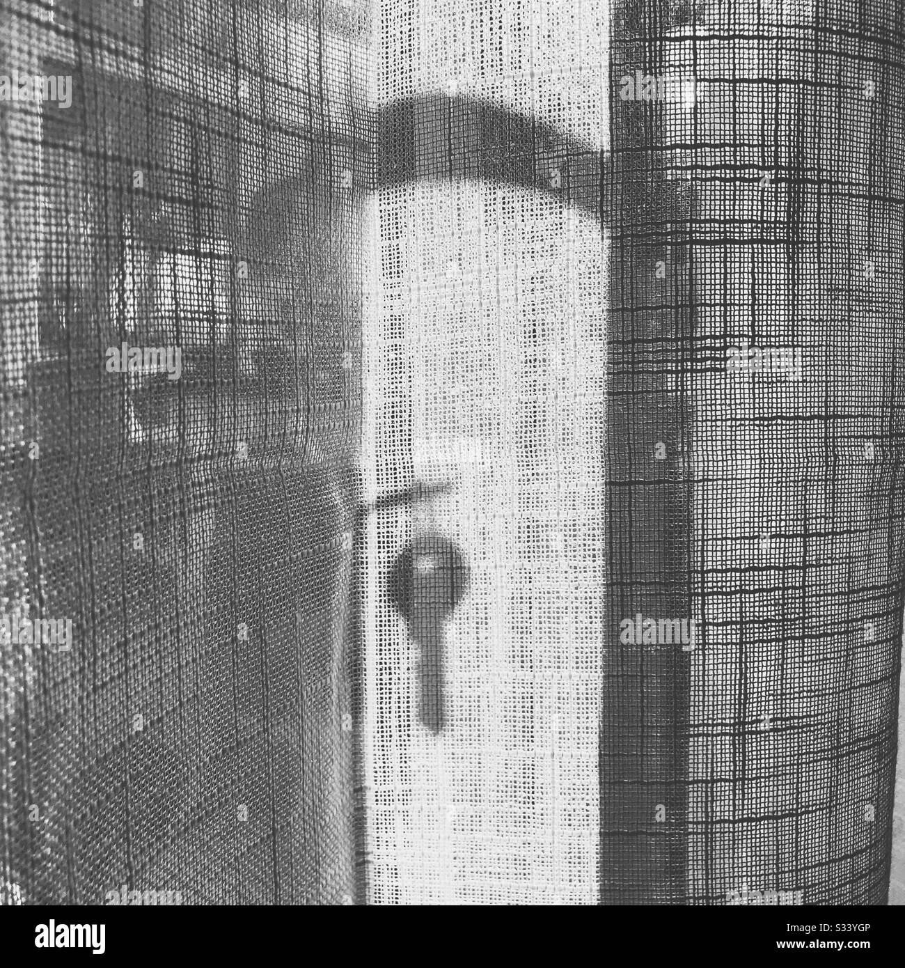 Ein Schlüssel, der hinter einem weißen Gazen-Netzvorhang vor den französischen Türen von einem Schloss im Silhouettenschatten aufgehängt ist Stockfoto