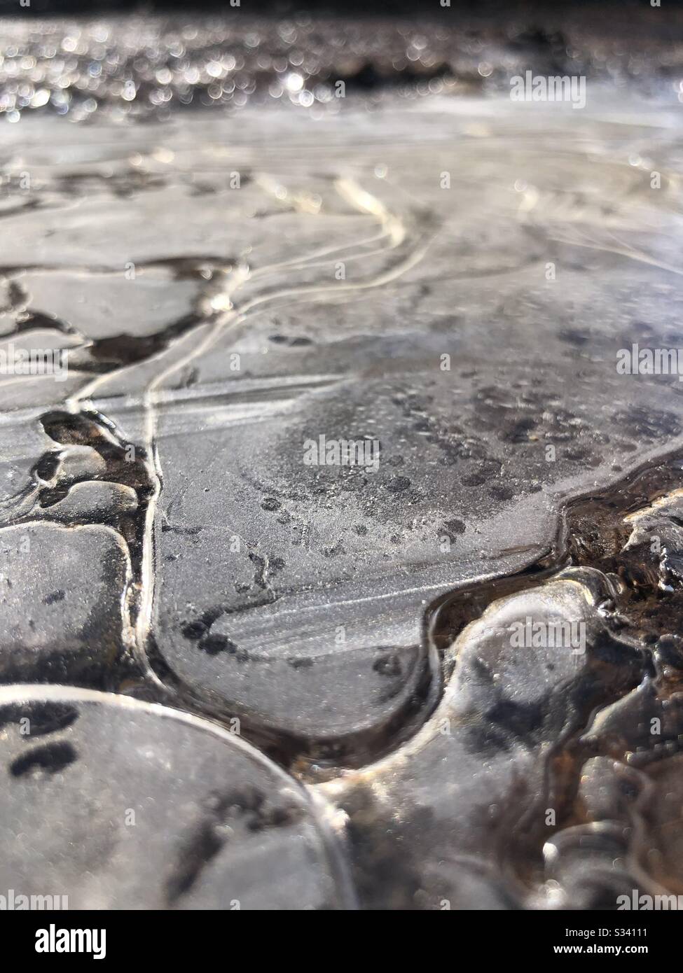 Eis schmilzt in der Sonne an einer gefrorenen Pfütze. Stockfoto