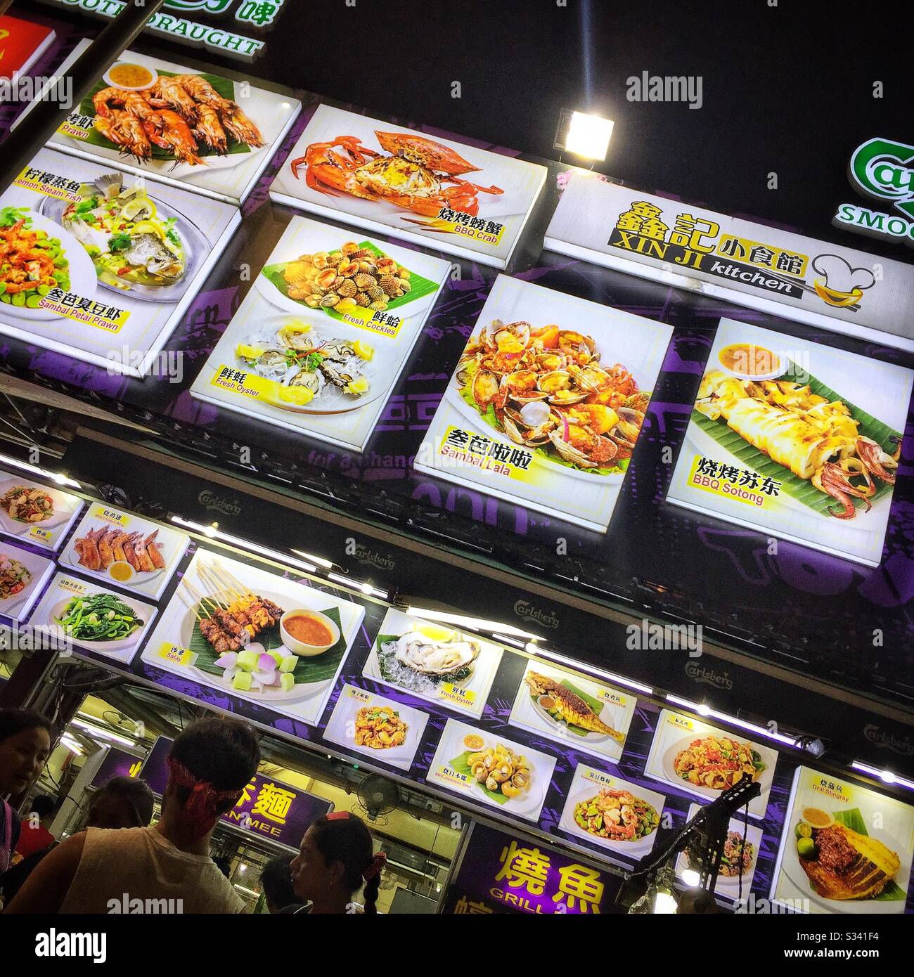 Beleuchtete Schilder zeigen Gerichte, die in einem Straßenrestaurant in Jalan Alor, einem Lebensmittelmarkt in Bukit Bintang, Kuala Lumpur, Malaysia, erhältlich sind - Smartphone-aufgenommenes Stockfoto