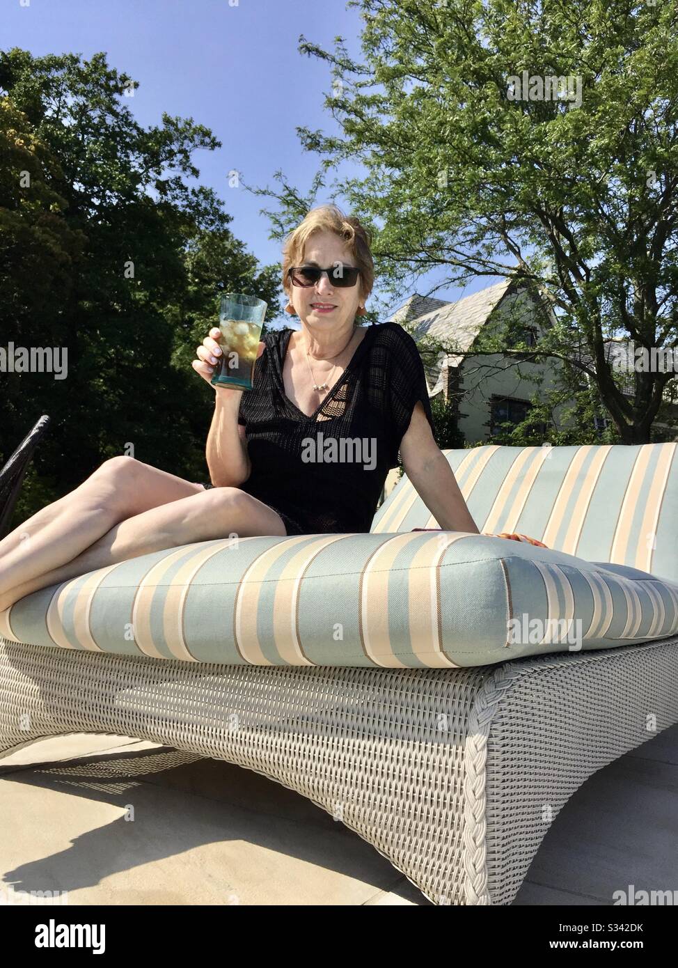 Frau in ihren 60er Jahren, die sich bei einem Drink in einem Ruhesessel auf einer Terrasse entspannen konnte - Smartphone-aufgenommenes Stockfoto