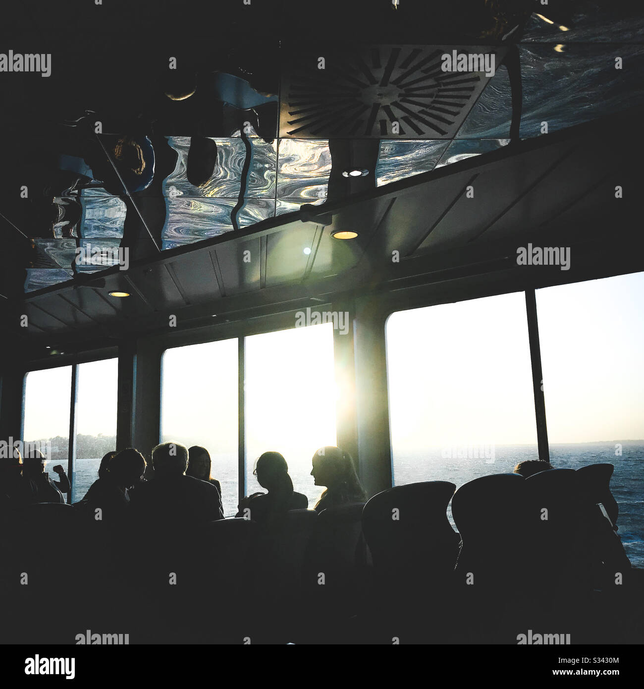 Sitzpassagiere in Silhouette auf der Fährüberfahrt zur Insel der Wight untergehenden Sonne, die durch Fenster, die hell über dem fernen Horizont leuchten, strahlt Stockfoto