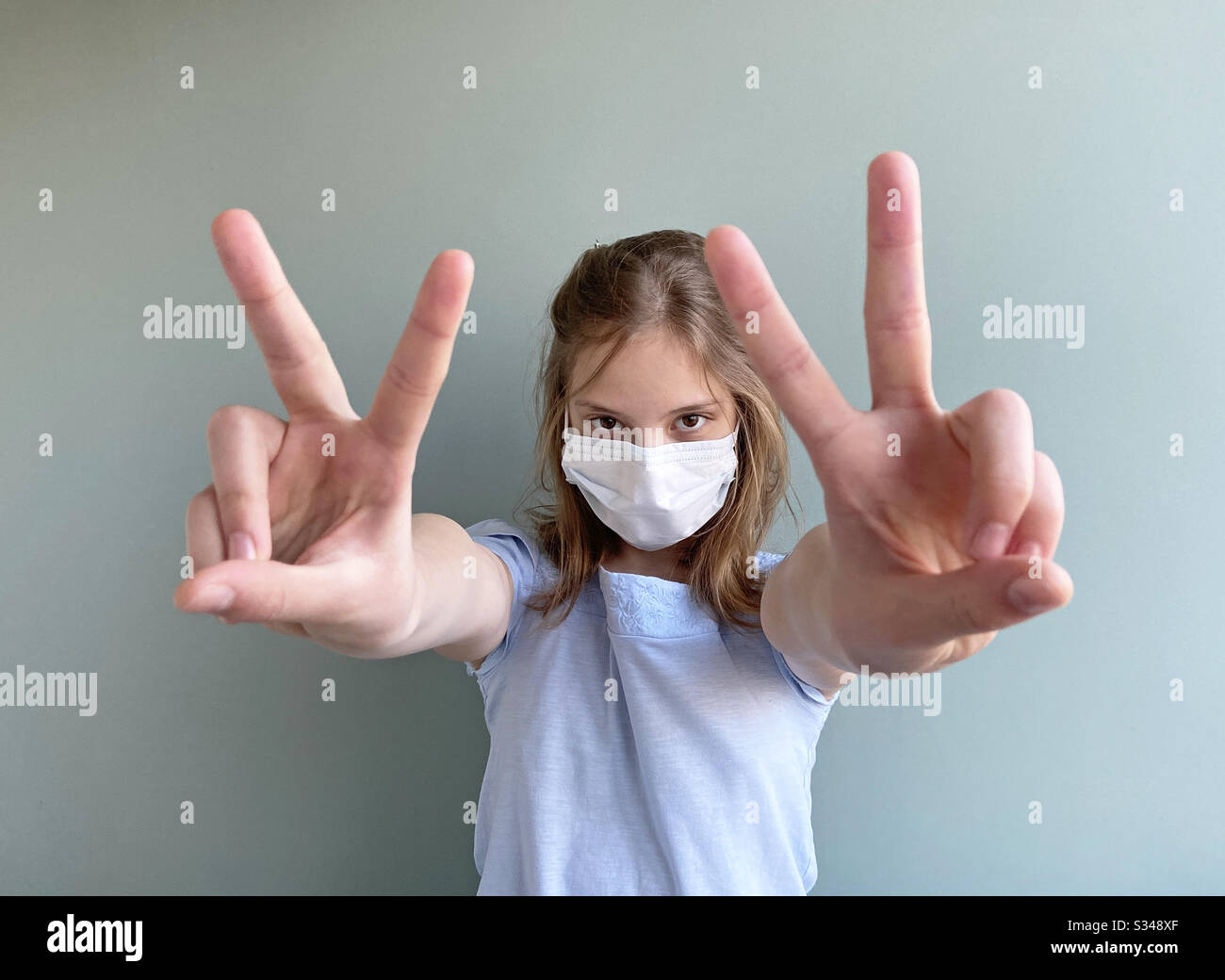 Siegesschild des Mädchens, das eine chirurgische Maske trägt - Smartphone-aufgenommenes Stockfoto