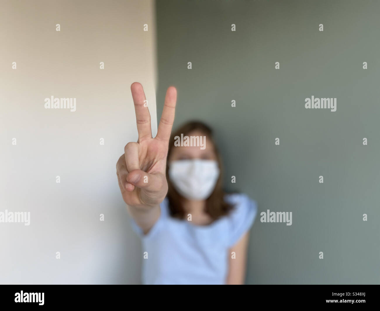 Siegesschild des Mädchens, das eine chirurgische Maske trägt - Smartphone-aufgenommenes Stockfoto