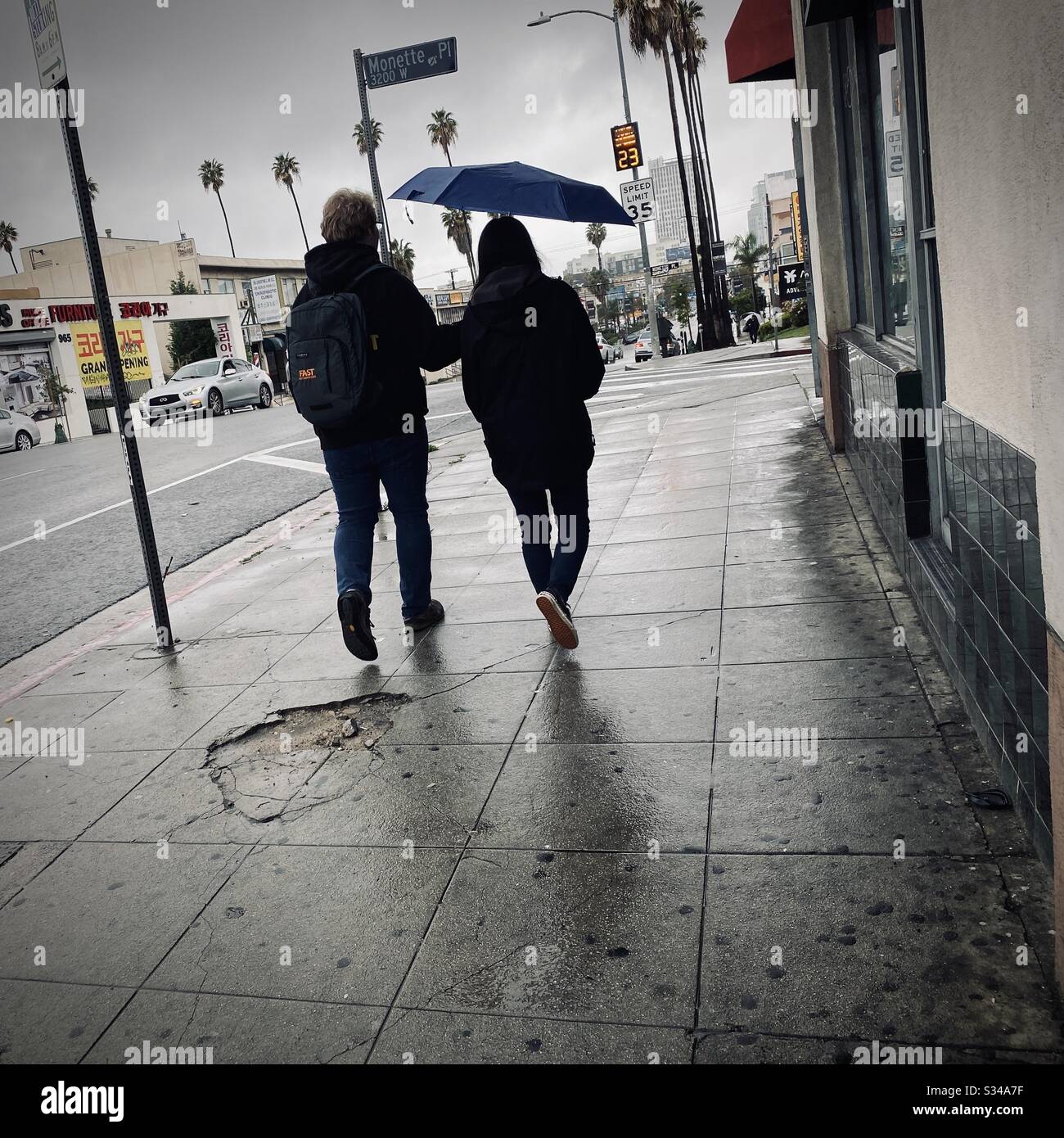LOS ANGELES, CA, MAR 2020: Junges Paar mit Mann, das Regenschirm über seiner Freundin trägt, während sie durch nasse Straßen in Korea-Stadt laufen Stockfoto