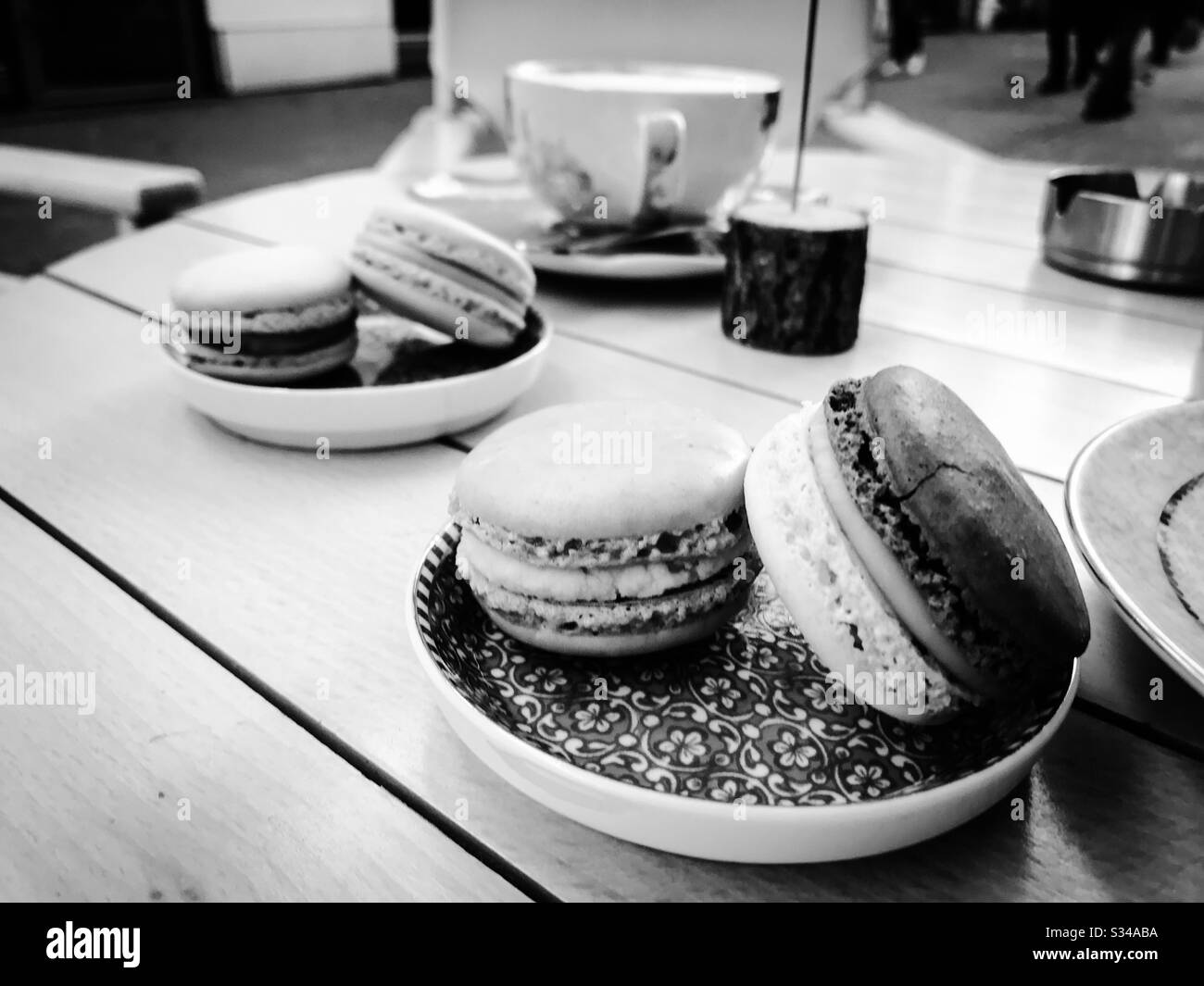 Kaffeetasse und zwei Teller mit Makronen auf einem Tisch in einem Café - schwarz und weiß Stockfoto