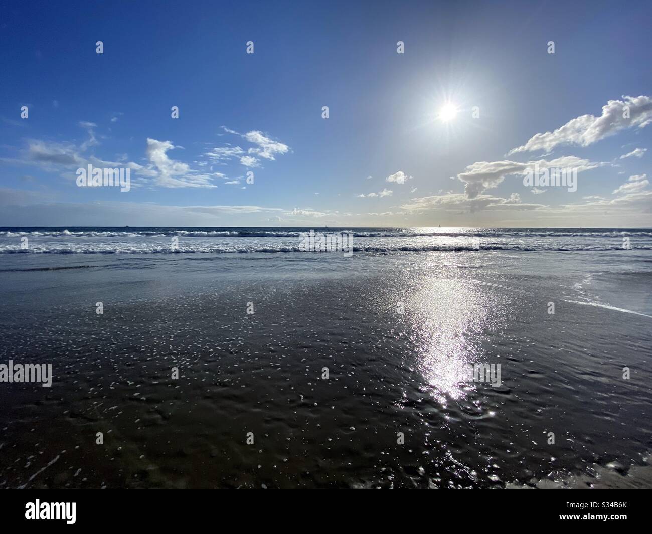 Außermittige Landschaft mit niedriger Sonne über dem Pazifischen Ozean und spärlichen Wolken im blauen Himmel rollen sanfte Wellen im Vordergrund Stockfoto