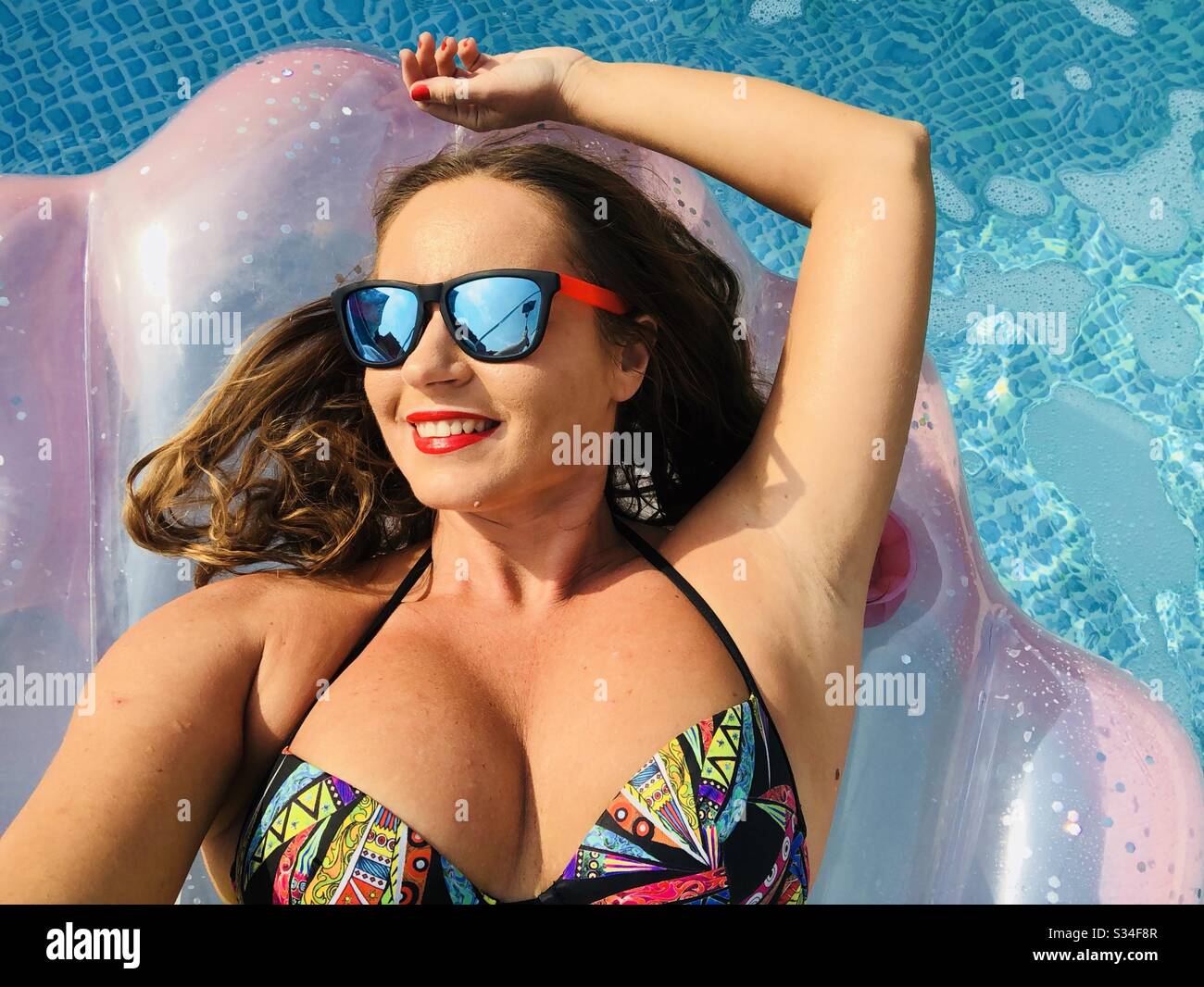 Frau, die Sonnenbrille auf einer aufblasbaren Poolmatratze trägt - Smartphone-aufgenommenes Stockfoto