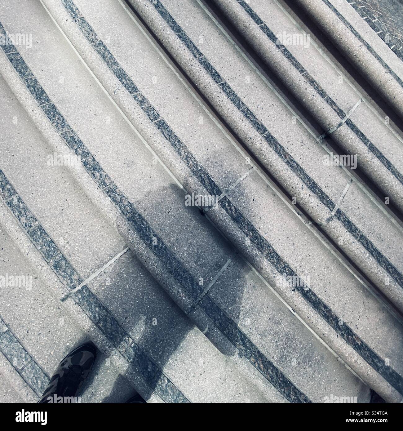 Der Schatten der Person fällt über einen Satz gebogener Stufen, umrandet mit schwarzen Steinen, draußen, tagsüber - Smartphone-aufgenommenes Stockfoto