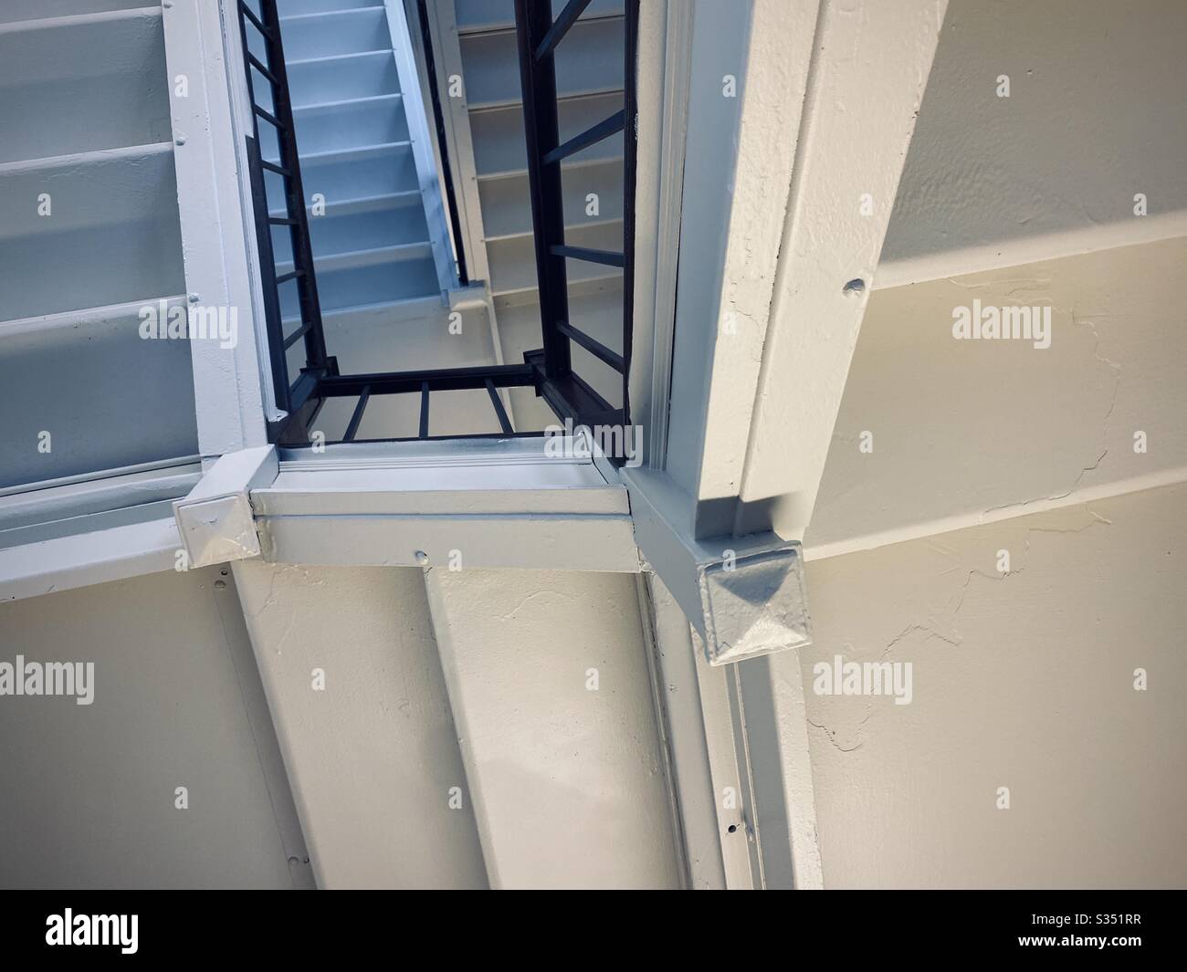 Weiß gestrichene Innenunterseite, Treppenhaus mit Bannister und blauem Tageslicht aus dem Fenster der oberen Ebene, das abstraktes Muster schafft Stockfoto