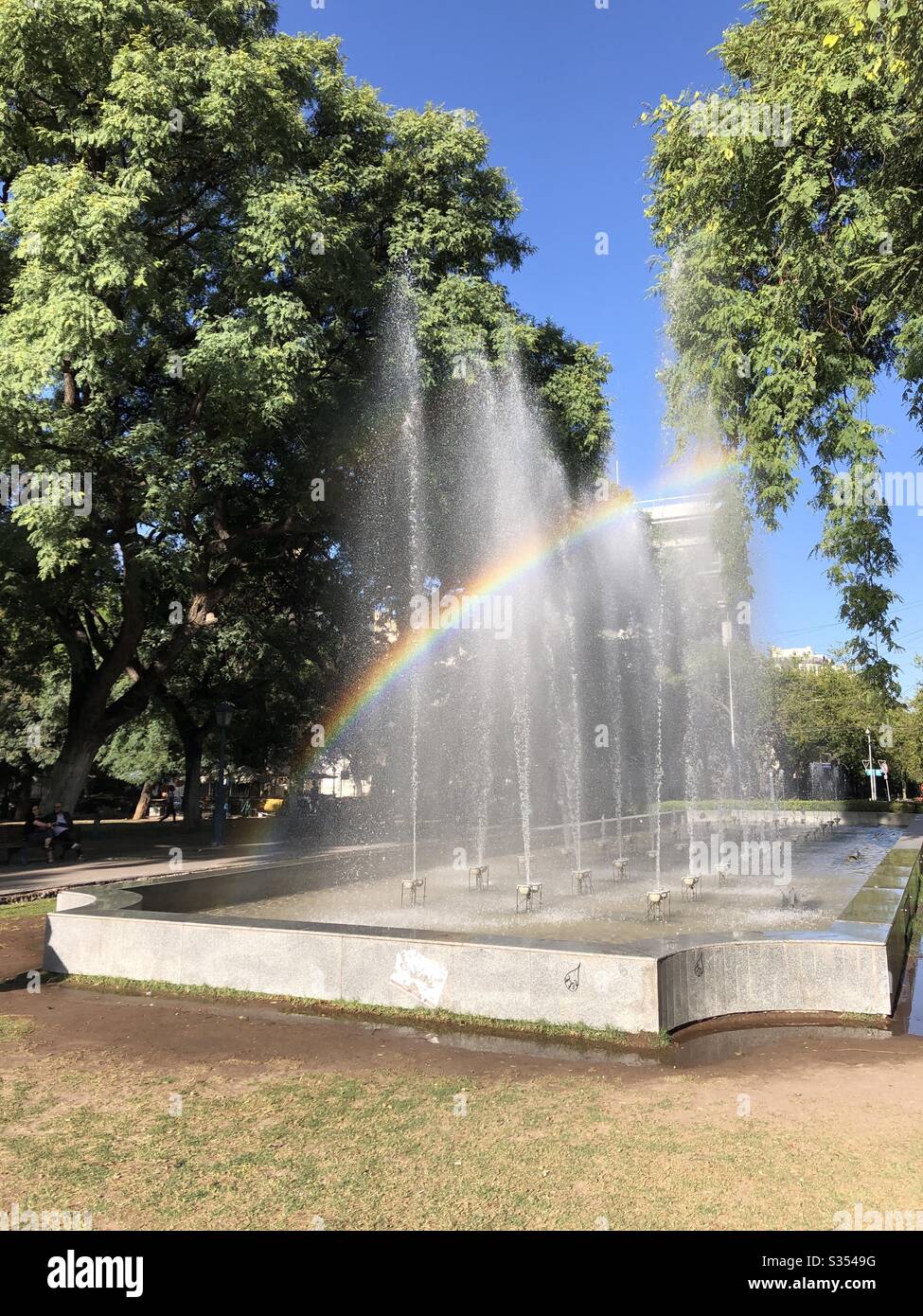 Ein Regenbogen erscheint in einem Wasserbrunnen in einem Park in Mendoza, Argentinien. - Smartphone-aufgenommenes Stockfoto