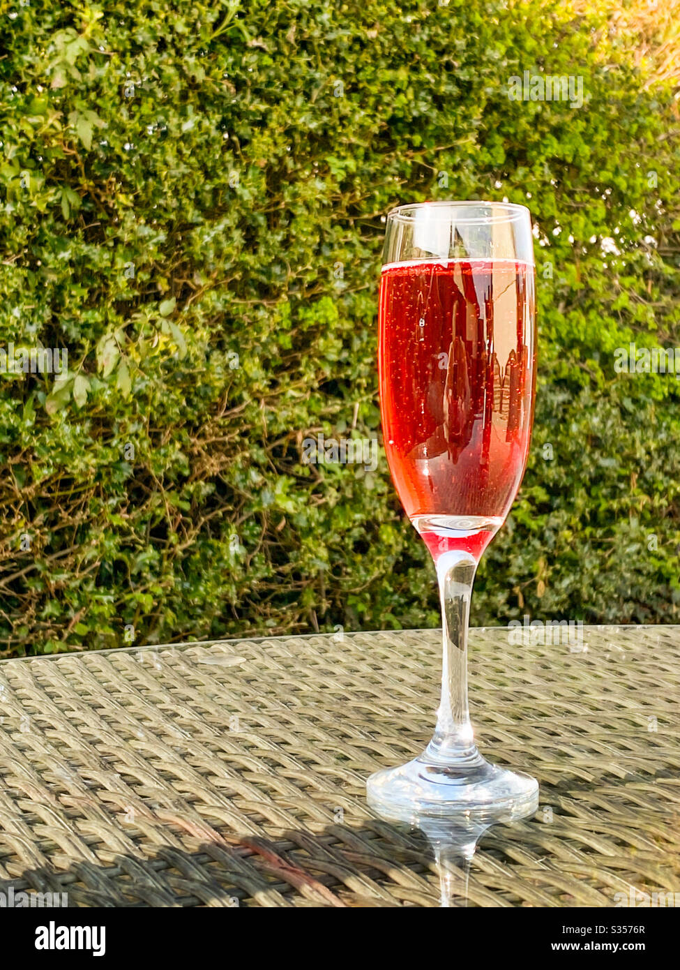 Ein Glas mit einer Flöte aus rosa Champagner auf der Glasplatte eines Tisches in einem Garten an einem Sommerabend Stockfoto