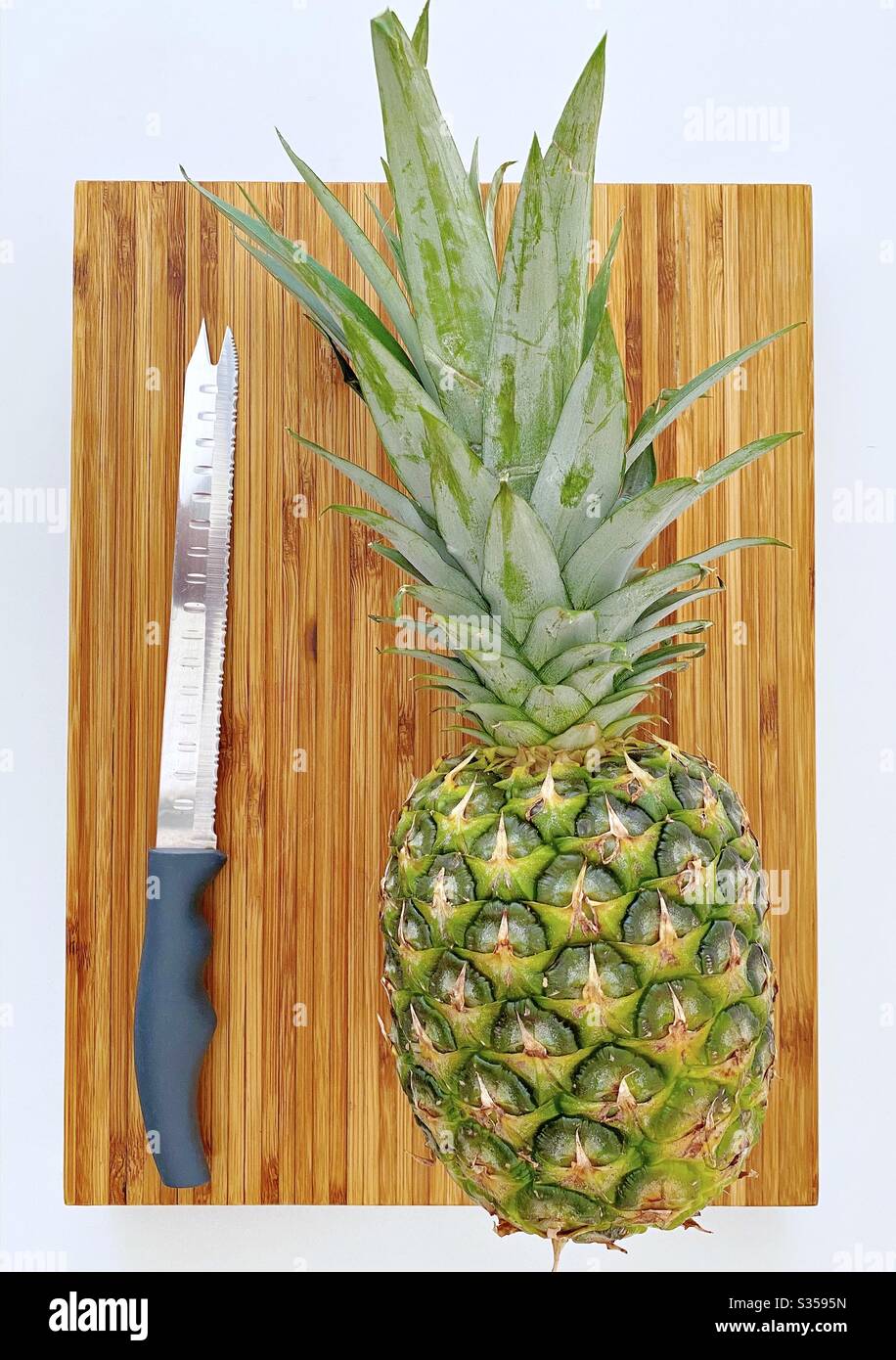 Eine ganze Ananas in der Küche zubereiten. Frische und reife Früchte. Zutaten für hausgemachte Ananassalsa. Auf einem Holzhackbrett mit Messer - Smartphone-aufgenommenes Stockfoto