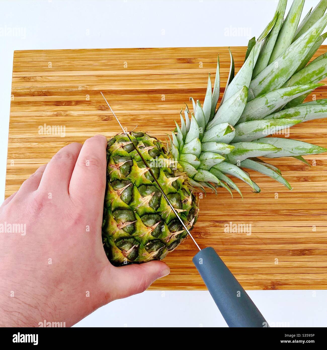 Eine ganze Ananas in der Küche zubereiten. Frische und reife Früchte. Zutaten für hausgemachte Ananassalsa. Auf einem Holzhackbrett mit Messer - Smartphone-aufgenommenes Stockfoto
