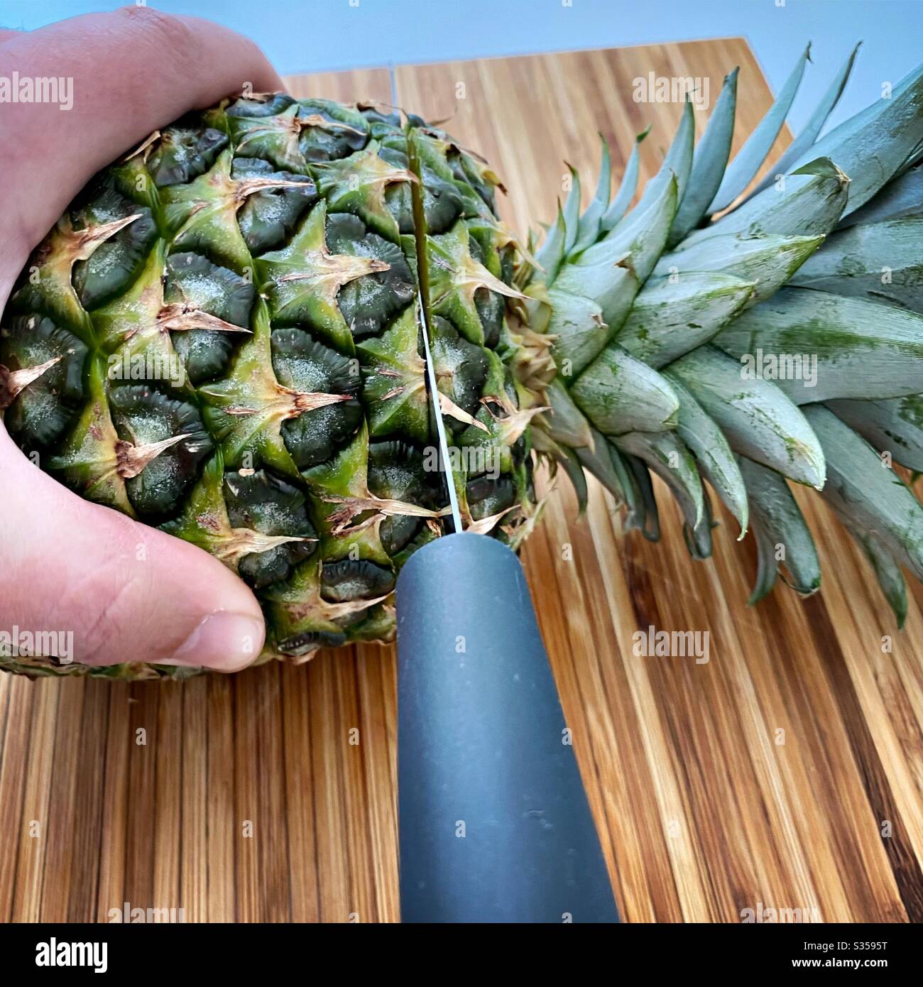 Eine ganze Ananas in der Küche zubereiten. Frische und reife Früchte. Zutaten für hausgemachte Ananassalsa. Auf einem Holzhackbrett mit Messer - Smartphone-aufgenommenes Stockfoto