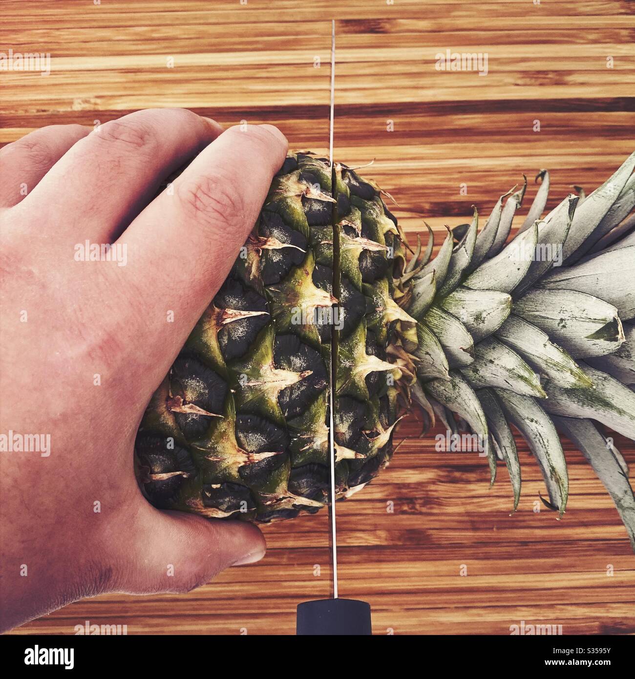 Eine ganze Ananas in der Küche zubereiten. Frische und reife Früchte. Zutaten für hausgemachte Ananassalsa. Auf einem Holzhackbrett mit Messer - Smartphone-aufgenommenes Stockfoto