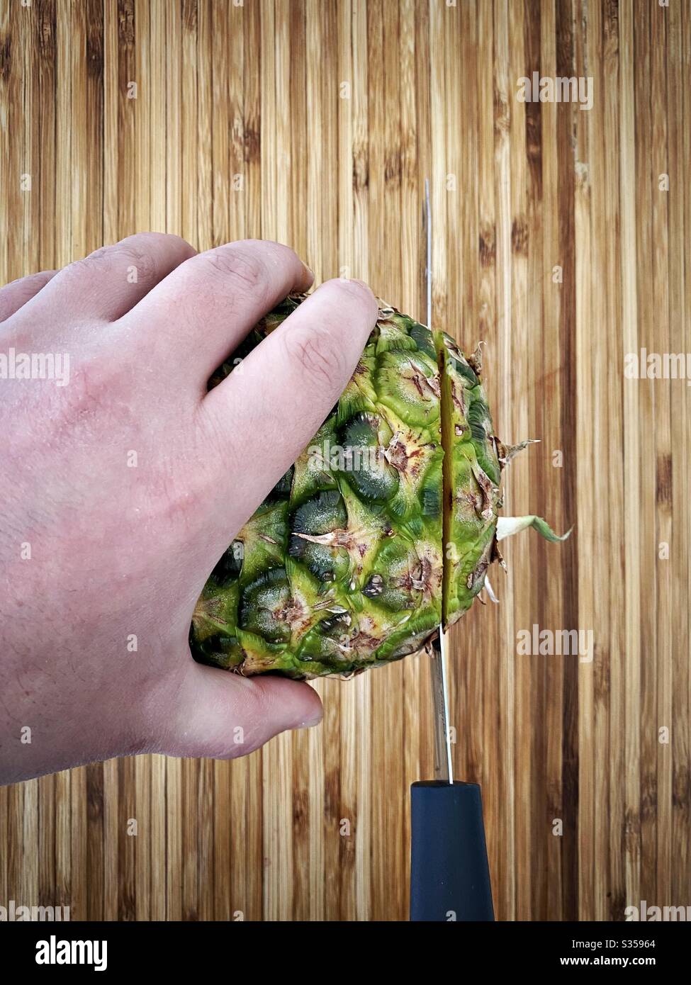 Eine ganze Ananas in der Küche zubereiten. Frische und reife Früchte. Zutaten für hausgemachte Ananassalsa. Auf einem Holzhackbrett mit Messer - Smartphone-aufgenommenes Stockfoto