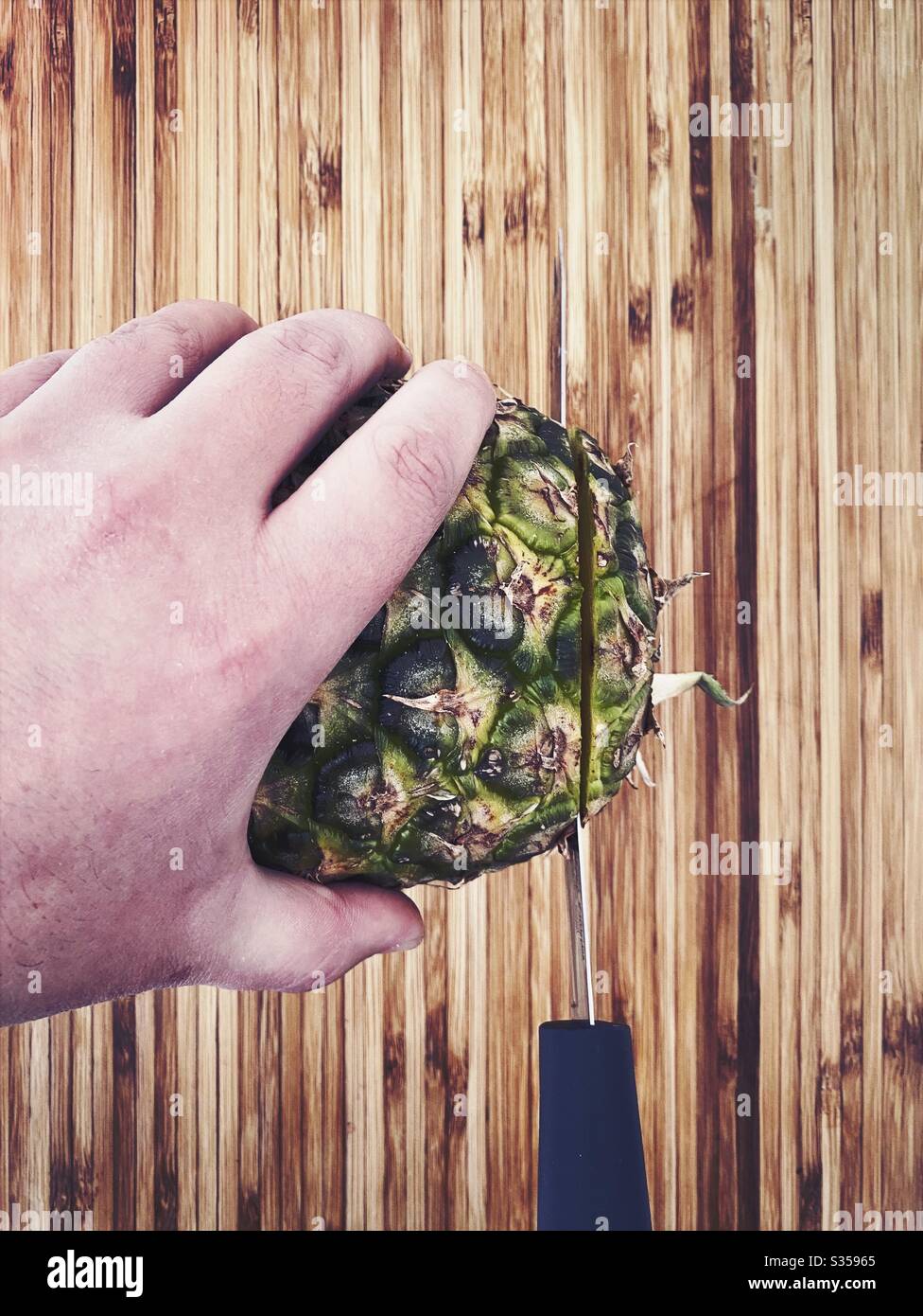 Eine ganze Ananas in der Küche zubereiten. Frische und reife Früchte. Zutaten für hausgemachte Ananassalsa. Auf einem Holzhackbrett mit Messer - Smartphone-aufgenommenes Stockfoto