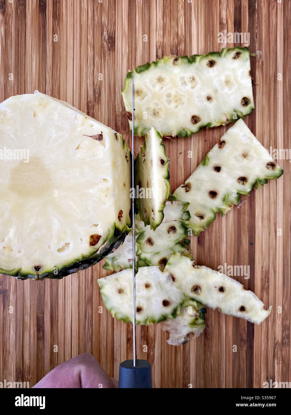 Eine ganze Ananas in der Küche zubereiten. Frische und reife Früchte. Zutaten für hausgemachte Ananassalsa. Haut auf einem Holzhackbrett mit Messer schälen - Smartphone-aufgenommenes Stockfoto