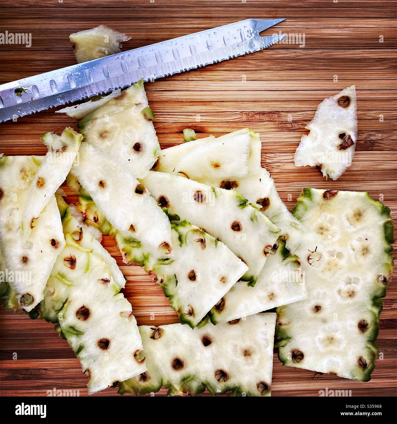 Eine ganze Ananas in der Küche zubereiten. Frische und reife Früchte. Zutaten für hausgemachte Ananassalsa. Geschälte Haut auf einem Holzhackbrett mit Messer - Smartphone-aufgenommenes Stockfoto