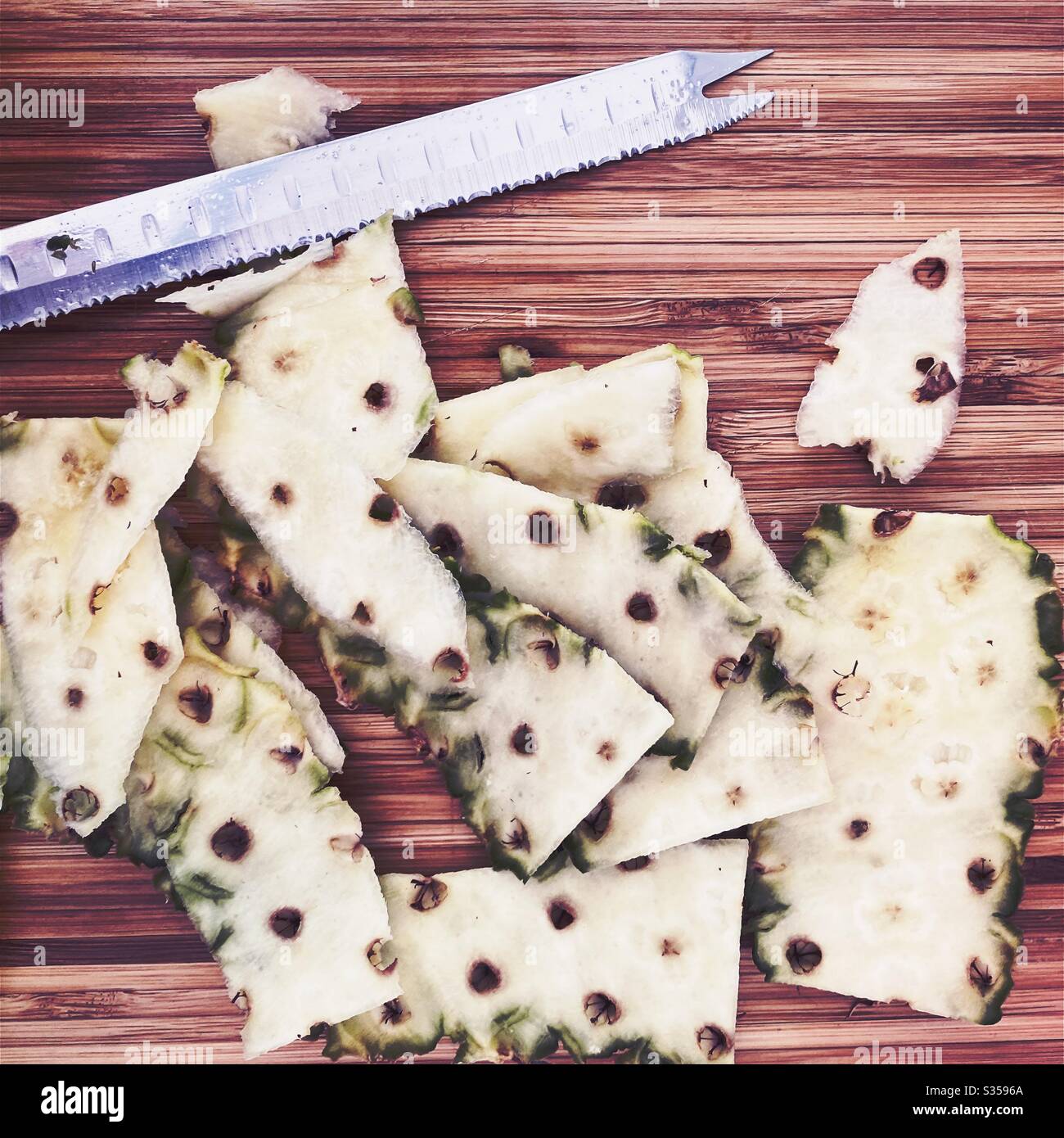 Eine ganze Ananas in der Küche zubereiten. Frische und reife Früchte. Zutaten für hausgemachte Ananassalsa. Geschälte Haut auf einem Holzhackbrett mit gezacktem Messer - Smartphone-aufgenommenes Stockfoto