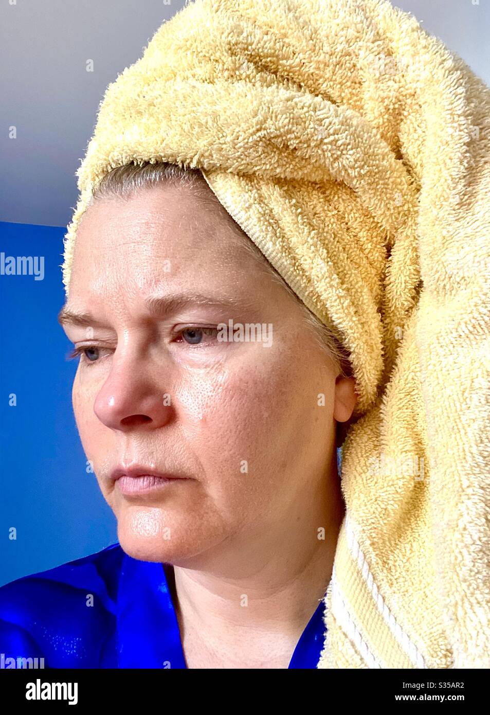 Frau mittleren Alters, die frisch mit einem gelben Handtuch auf ihrem nassen Haar geduscht wurde. Stockfoto