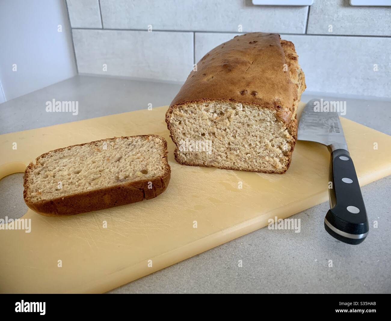 Hausgemachtes Bananenbrot auf einem Schneidebrett mit einem Messer. - Smartphone-aufgenommenes Stockfoto