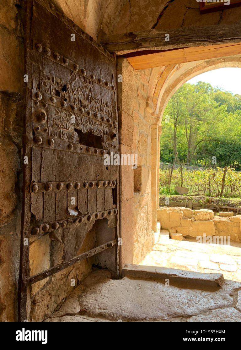 Eine sehr alte verfallende Metalltür mit großen Flüssen und georgischer Schrift. Vor der Kulisse eines Steingebäudes und Grünflächen. Kutaissi, Georgien. - Smartphone-aufgenommenes Stockfoto