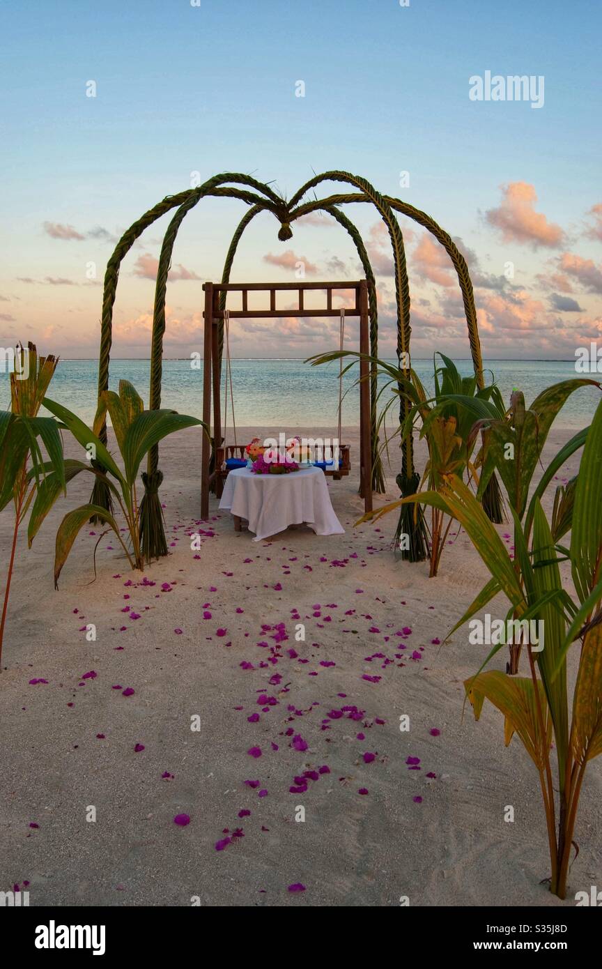 Hochzeitsarbour bei Sonnenuntergang auf den Malediven an einem weißen Sandstrand mit rosa Rosenblättern auf dem Sand verstreut. - Smartphone-aufgenommenes Stockfoto
