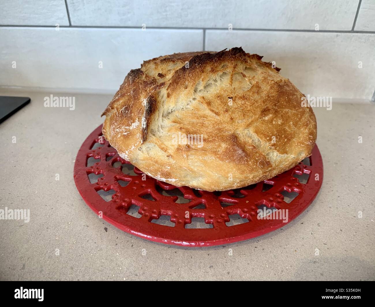 Knuspriger Laib Brot. Ein selbstgebasteltes Brot saß auf einem roten Kühlregal. - Smartphone-aufgenommenes Stockfoto