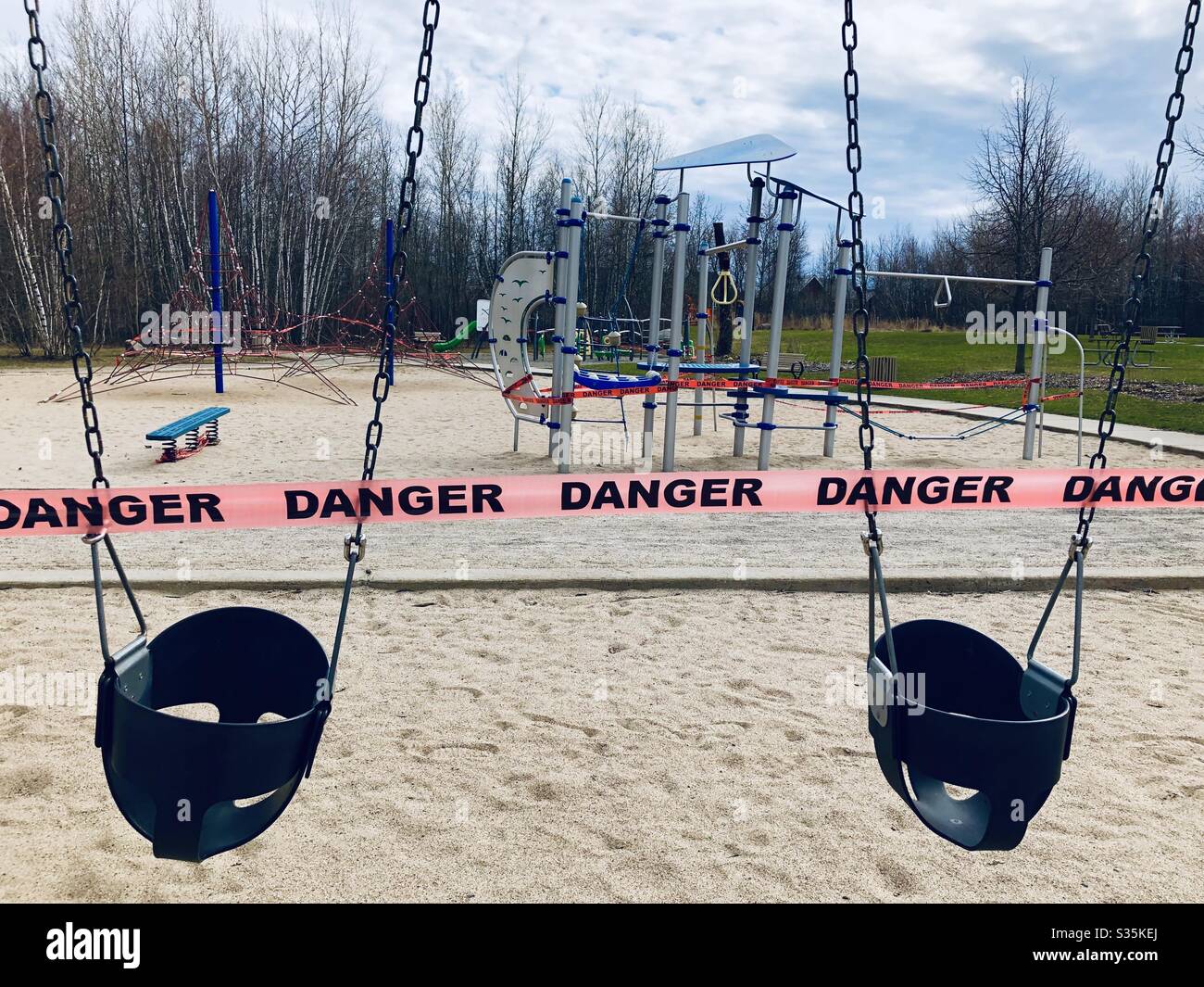 Spielplatz in einem Park, der durch ein Banner mit Gefahr während der covid 19 sozialen Distanzierung geschützt ist - Smartphone-aufgenommenes Stockfoto