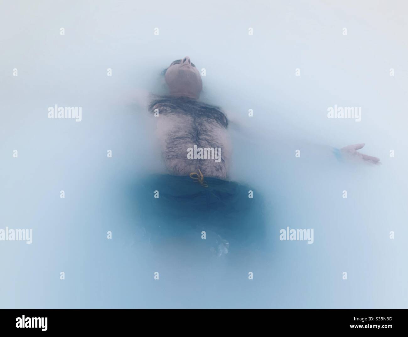 Mann schwimmt in einem milchigen geothermischen Pool. Entspannend und ruhig. Blaue Lagune, Island. Stockfoto