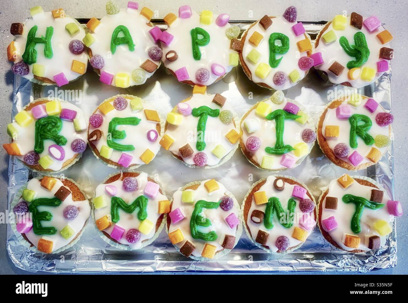 ‘Happy Retirement’ hausgemachte Kuchen, weiße Glasur mit grünen Hand paspelierten Schriftzug und bunten Süßigkeiten / Süßigkeiten. Stockfoto