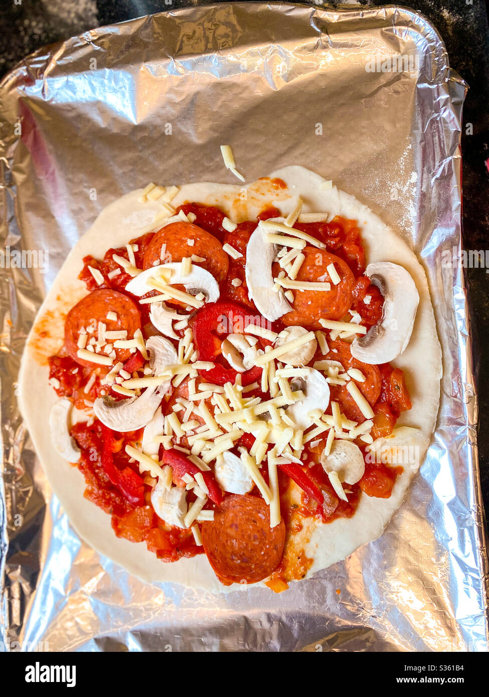 Tomate. Käse, Pepperoni, Pfeffer und Zwiebel Belag auf einer hausgemachten Pizza auf einem Backblech mit Blechfolie bedeckt. - Smartphone-aufgenommenes Stockfoto
