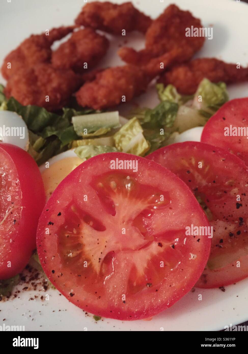 Ein Hauptgericht mit panierten, gebratenen Garnelen und einem frischen Gartensalat mit geschnittenen, von Weinreben gereiften Tomaten Stockfoto