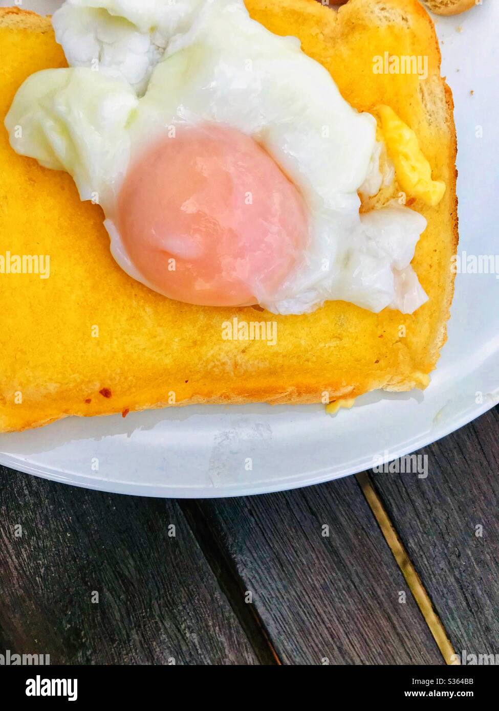 Pochiertes Ei auf weißem Toast mit Butter serviert Stockfoto